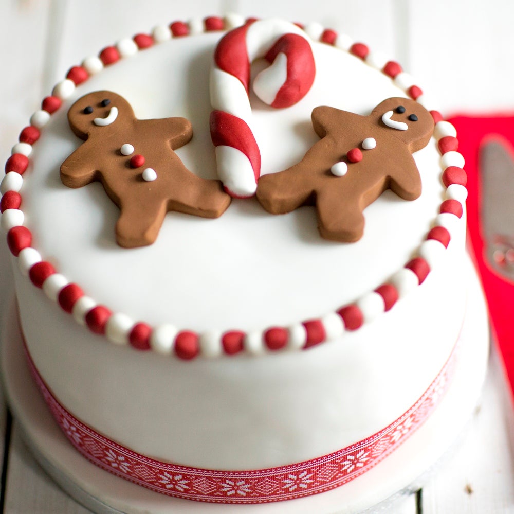 Christmas Cake decorated in white fondant with red ribbon and covered in fondant gingerbread men and candy canes