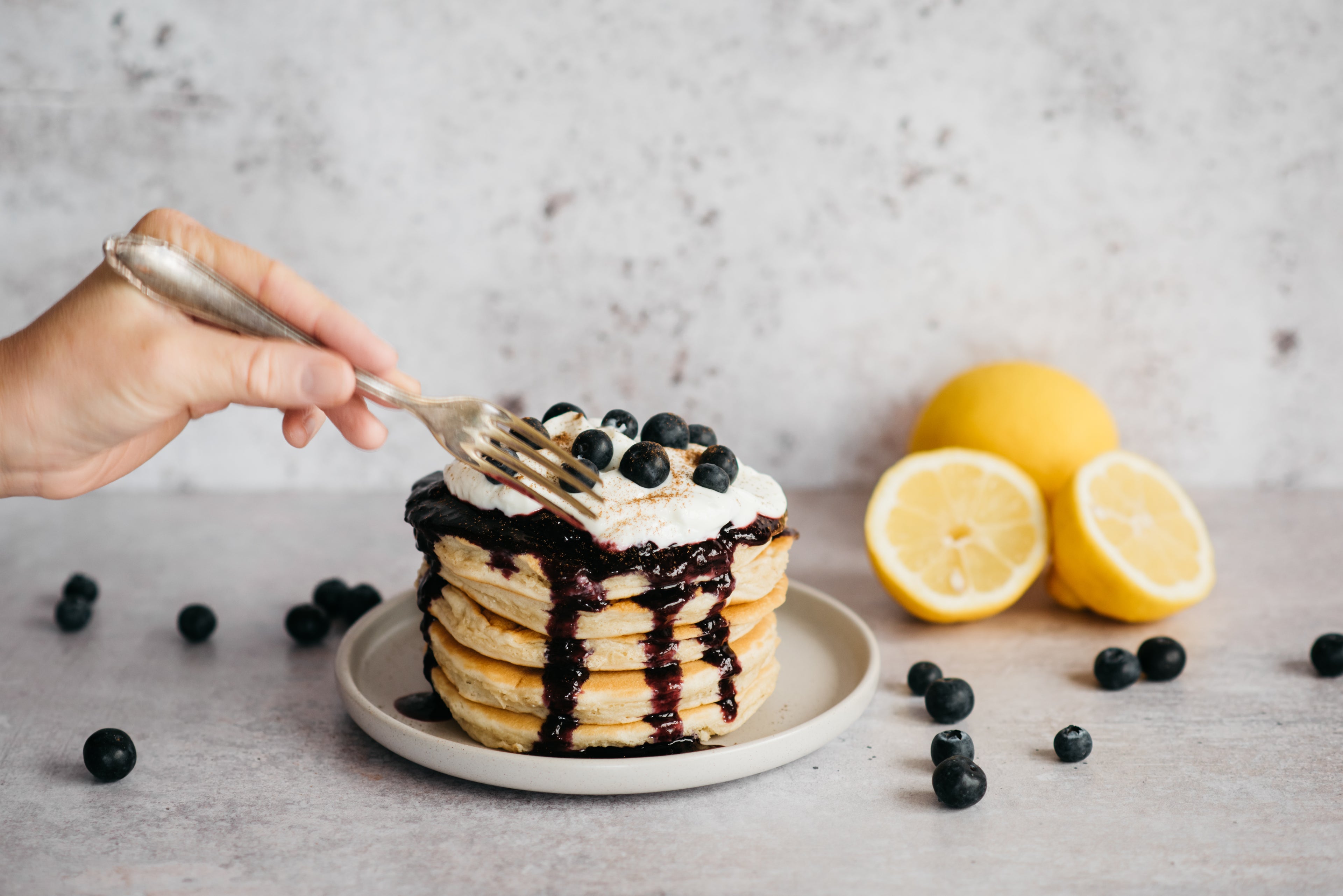 Stack of Cinnamon Pancakes with Blueberry Compote with a hand using a fork to slice into the pancakes