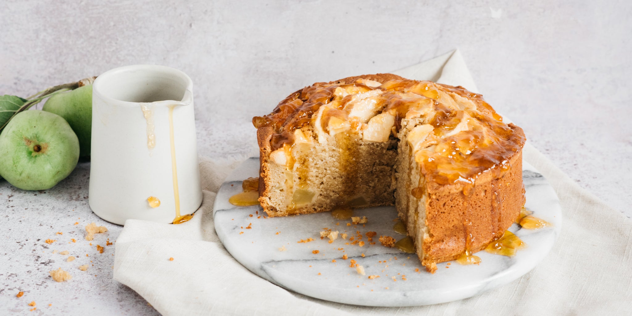 Apple cake with slice removed beside a jug and some apples