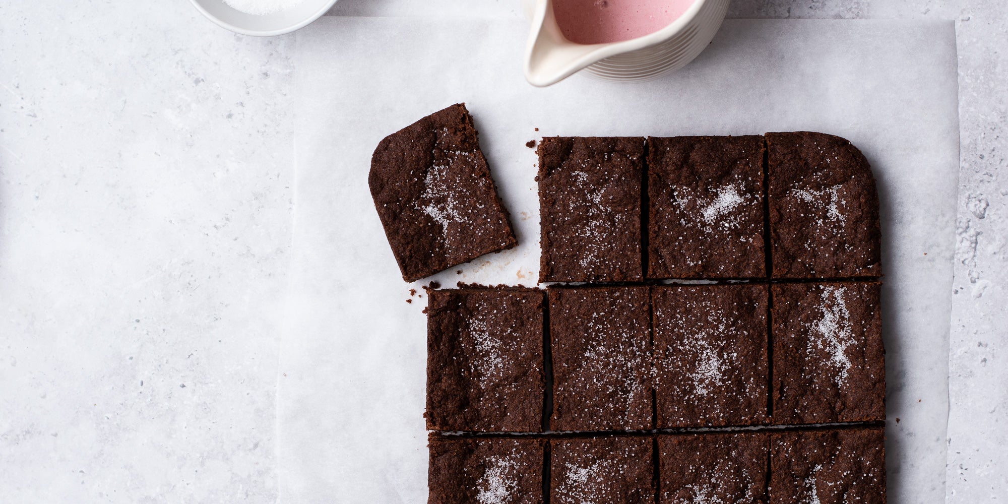 Overhead shot of chocolate concrete cake with square pull away and jug of pink custard