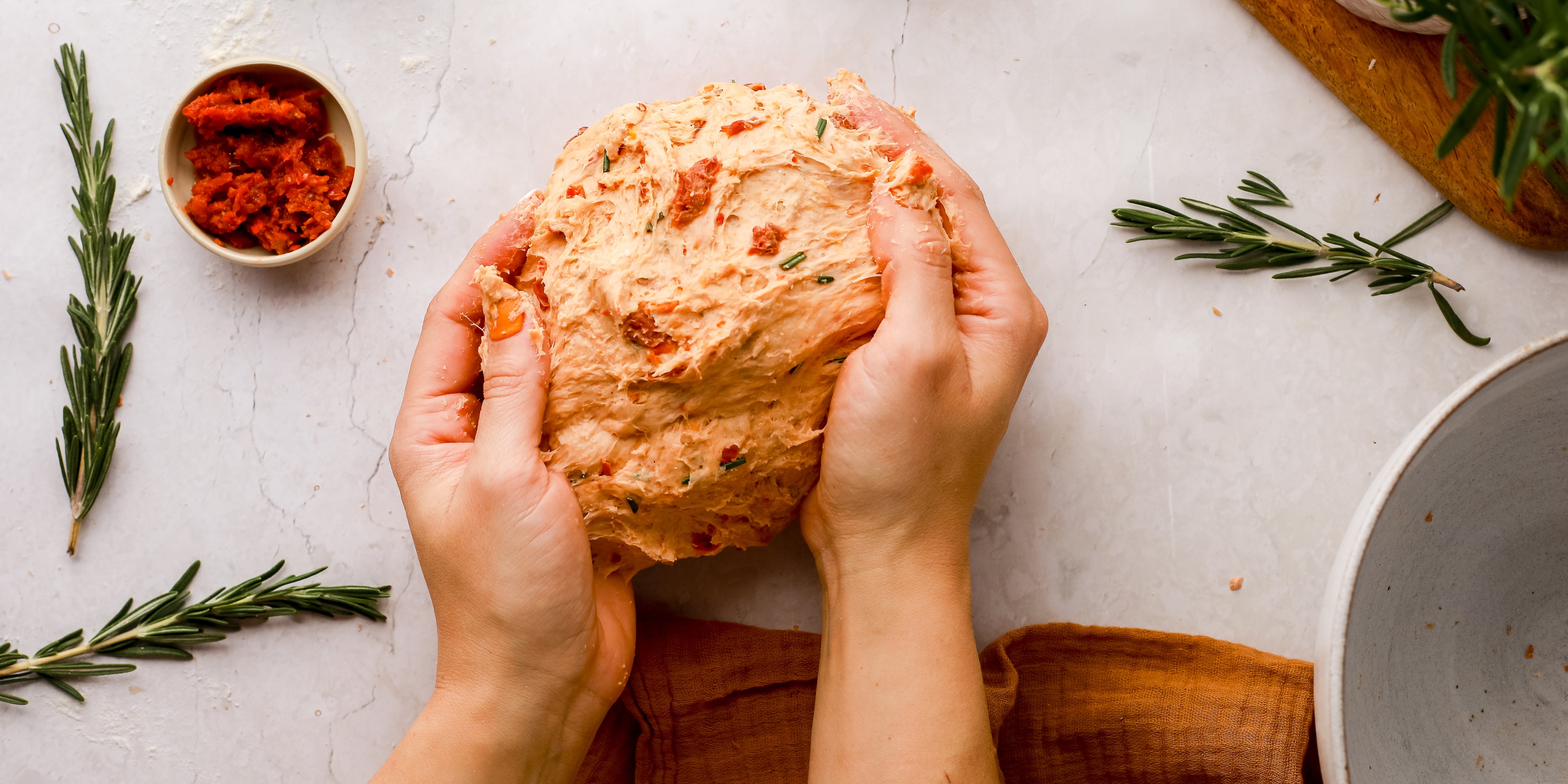 Kneading a ball of sundried tomato bread dough on a white kitchen surface