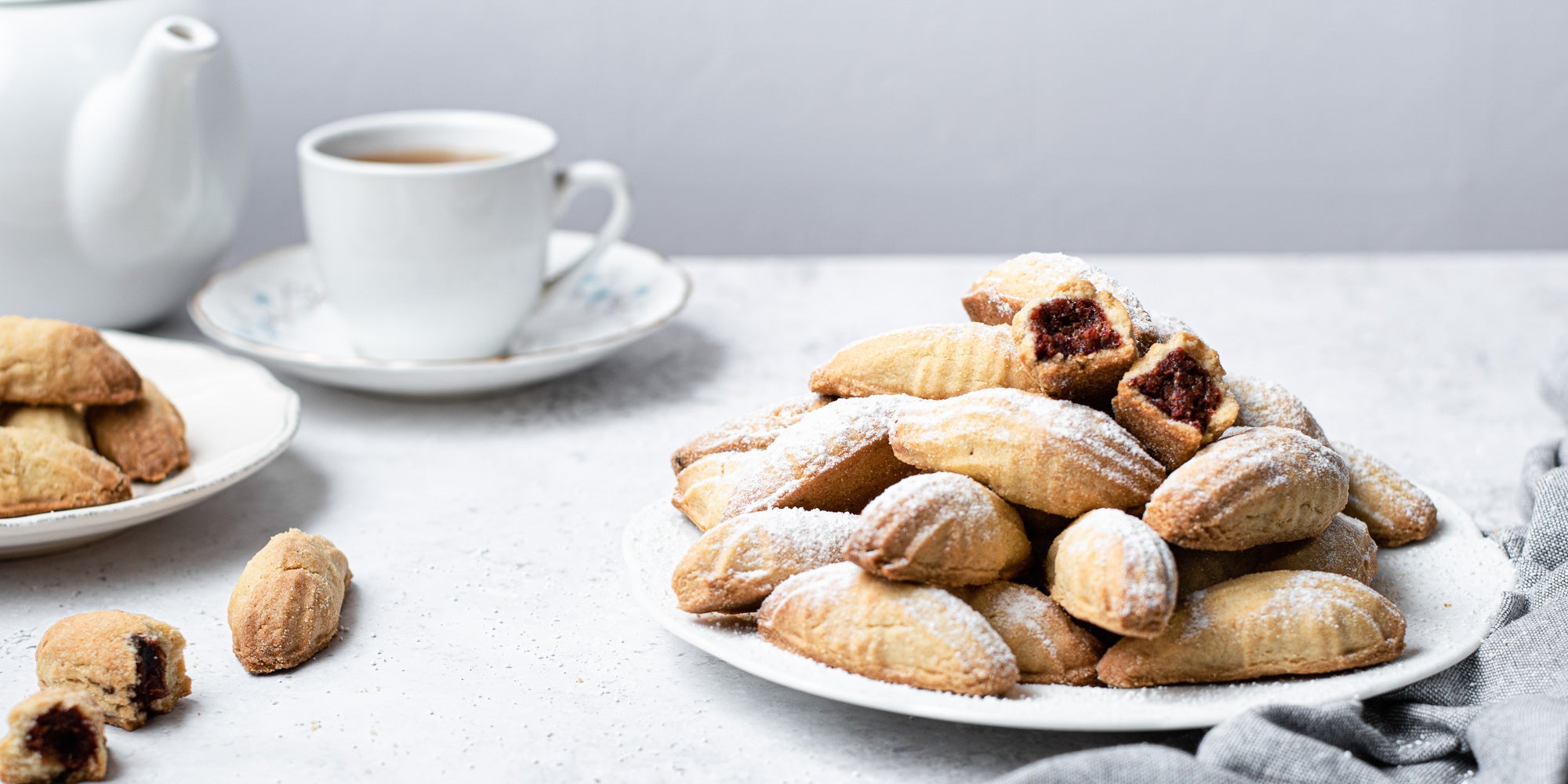 Mamoul cookies dusted with icing sugar, next to a pot of tea 