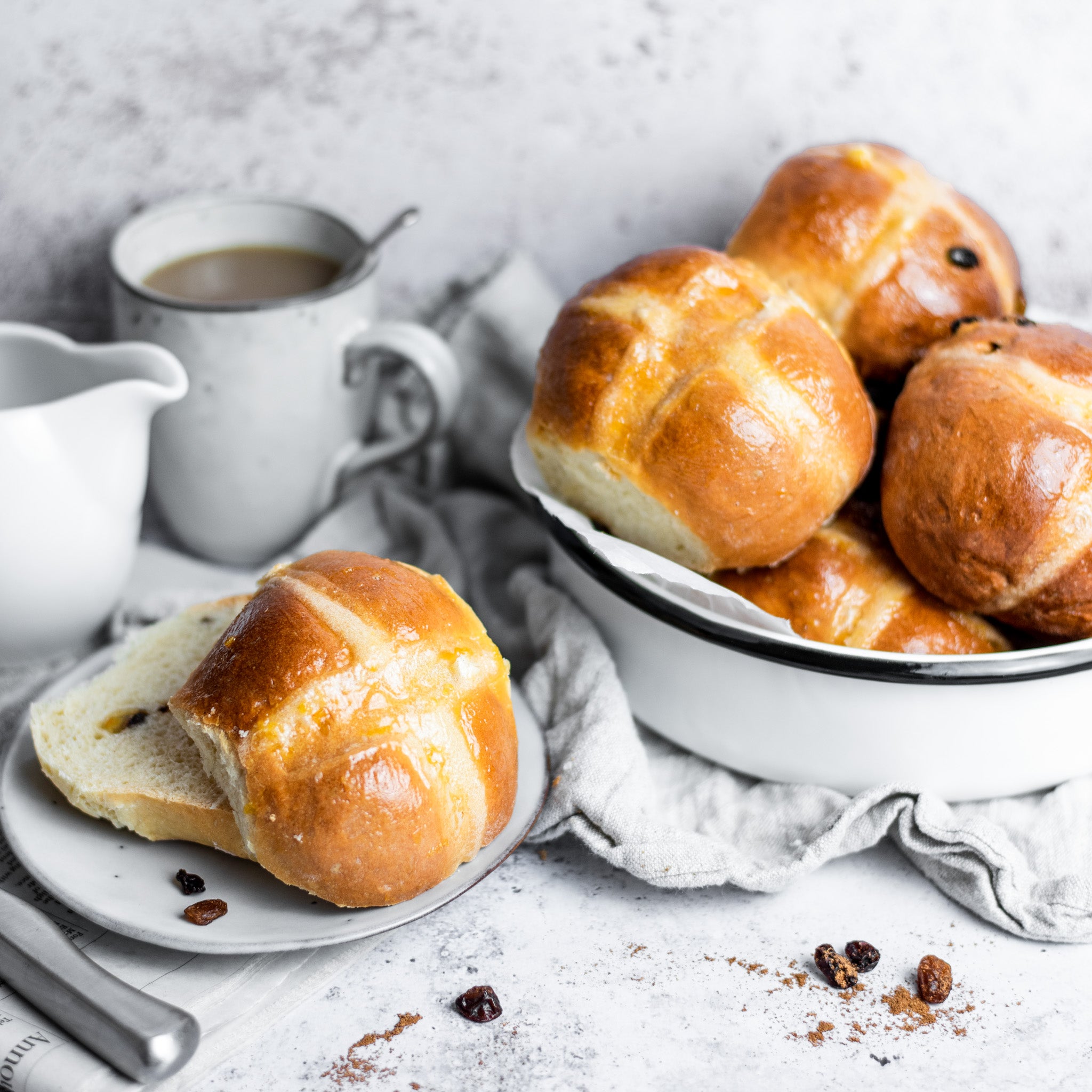 Sliced hot cross bun on a white plate next to a dish of hot cross buns