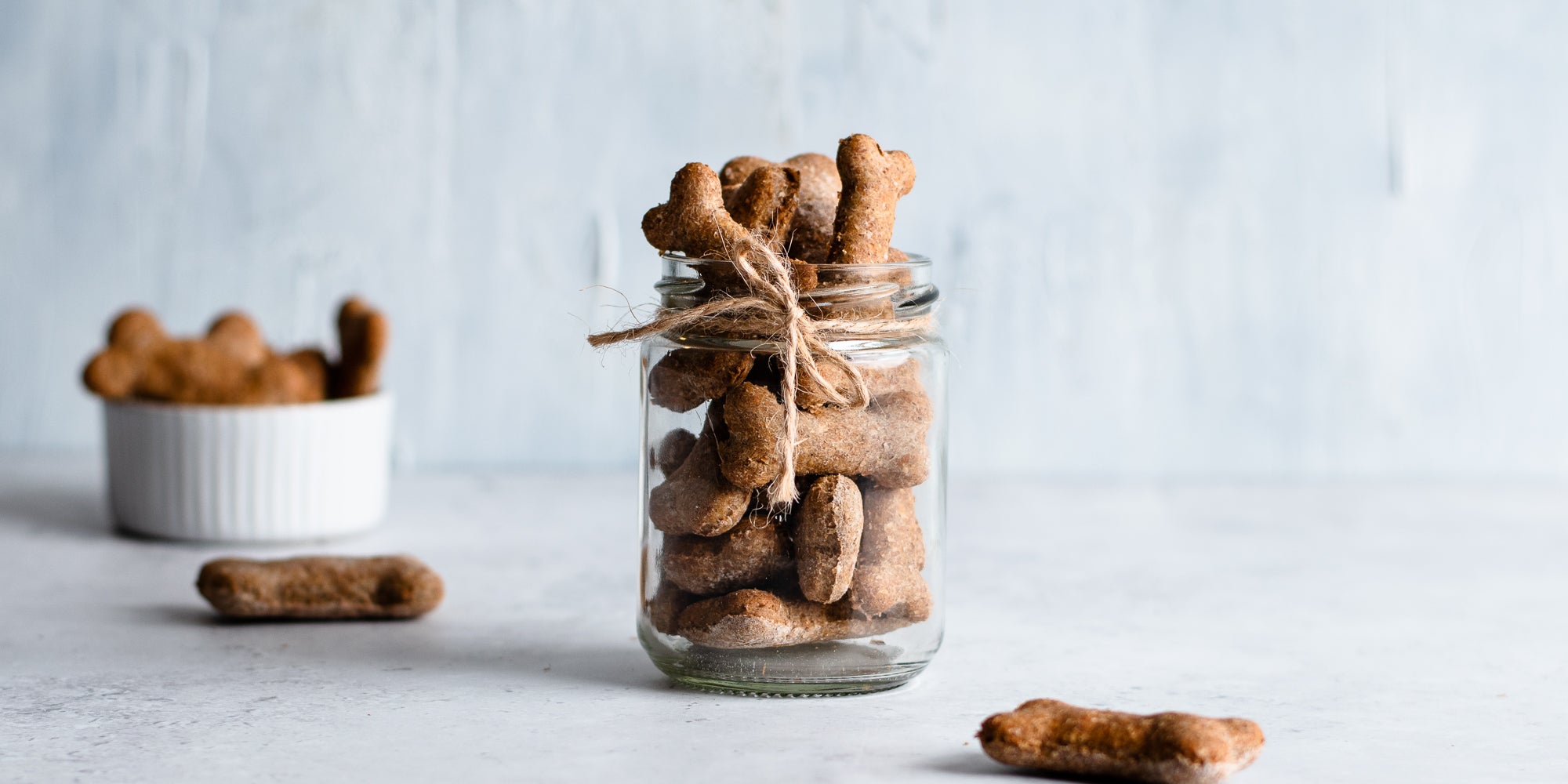 Dog Biscuits in a glass jar tied with twine with a ramekin of dog biscuits in the background
