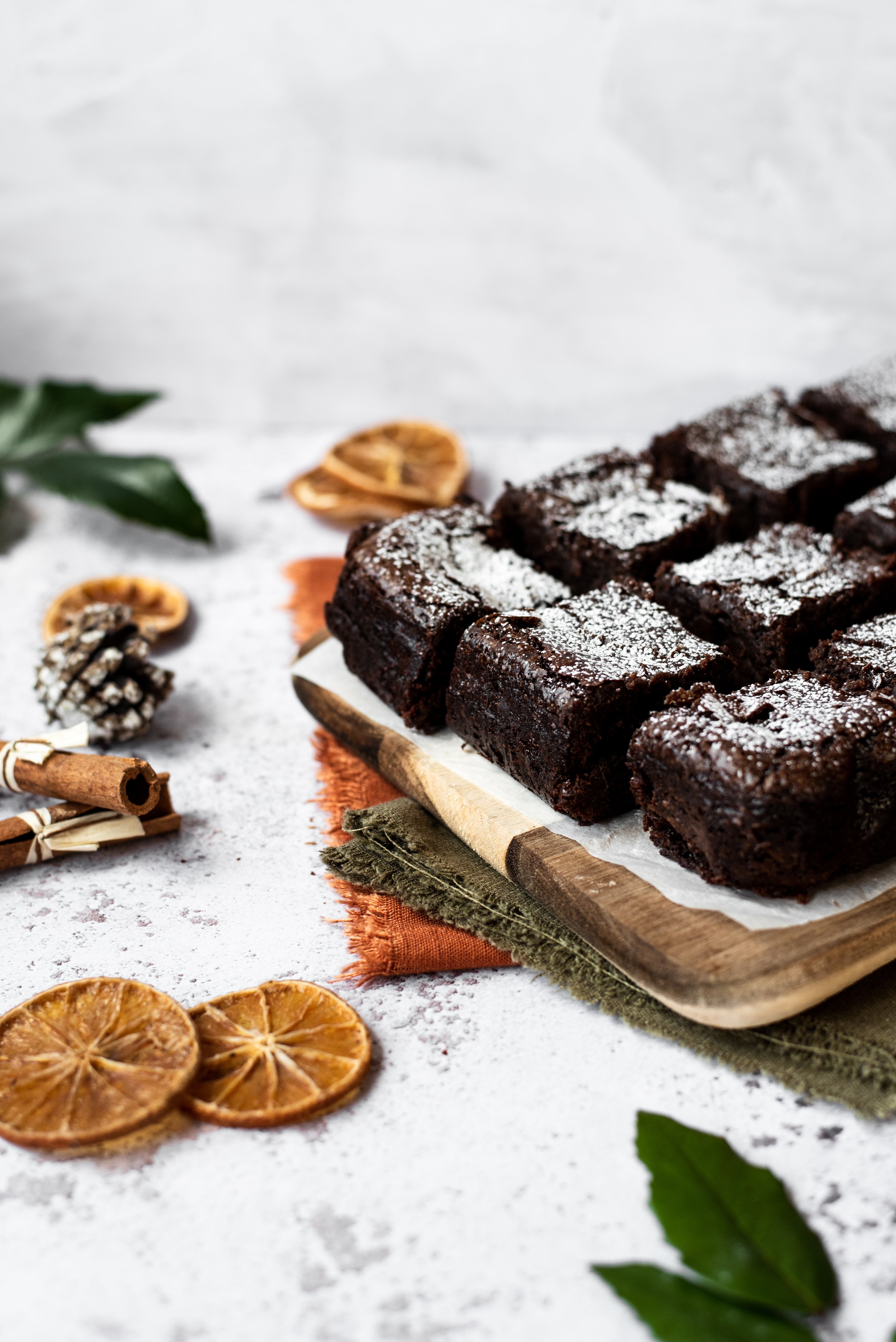 Brownie chopped into squares on chopping board with dried orange and cinnamon sticks