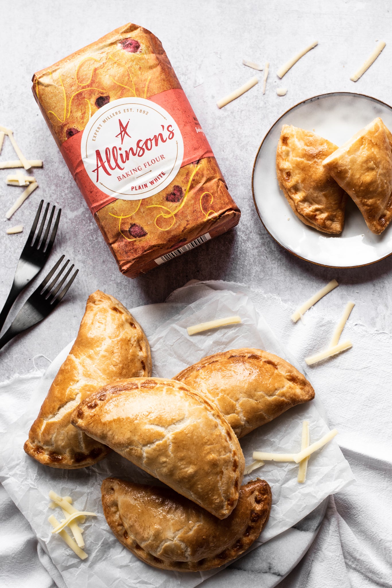 Pile of cheese & onion pasties, pack of flour, sprinkled cheese and one pasty sliced open