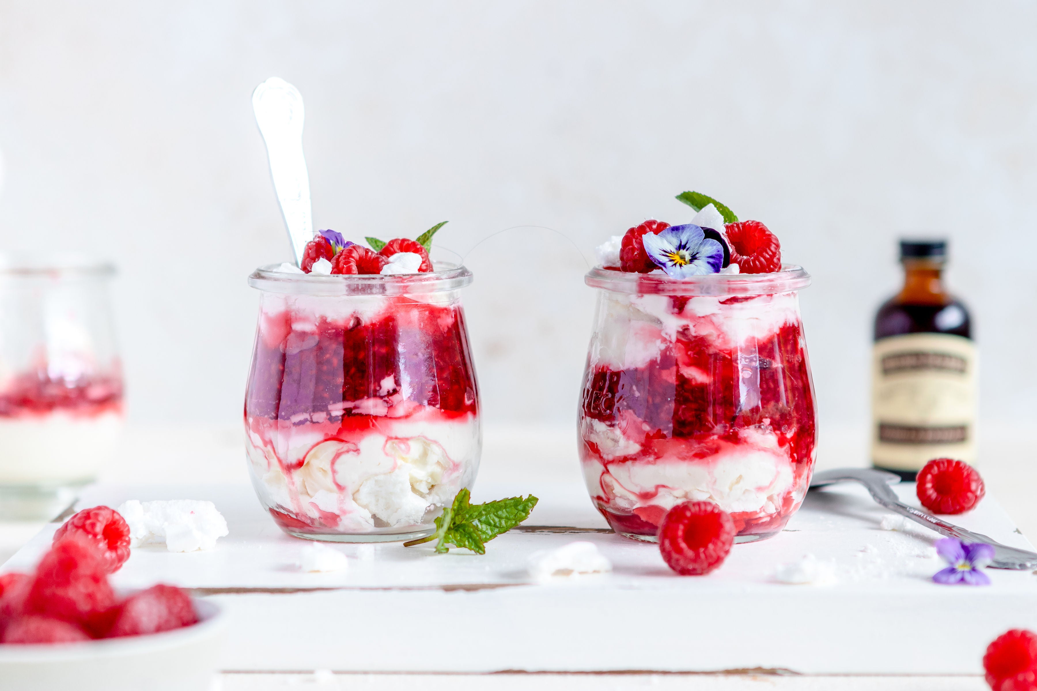 2 glass jars of eton mess, raspberries, edible flowers and vanilla extract