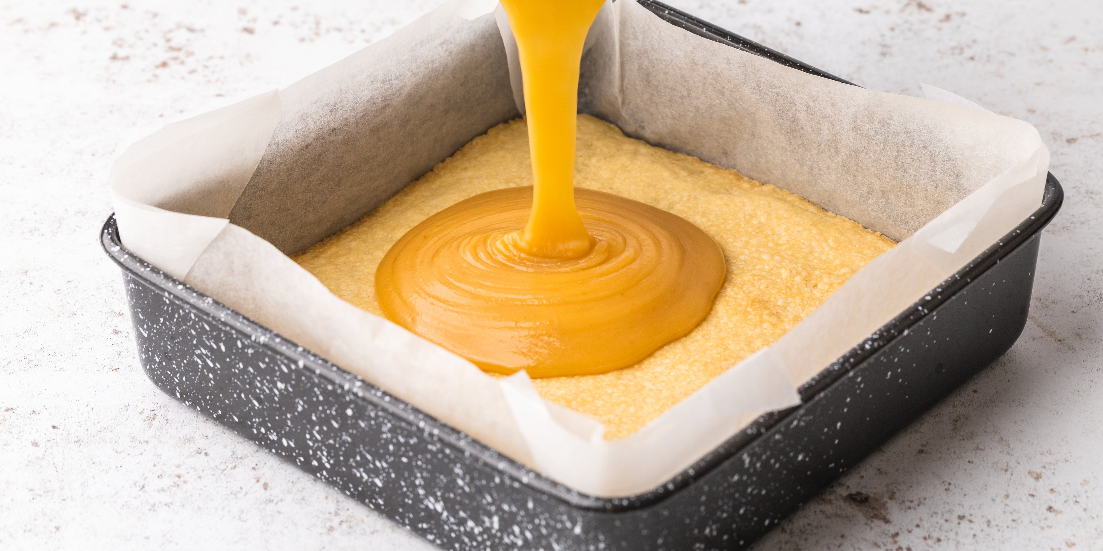 Caramel being poured on top of shortbread in a square baking tin