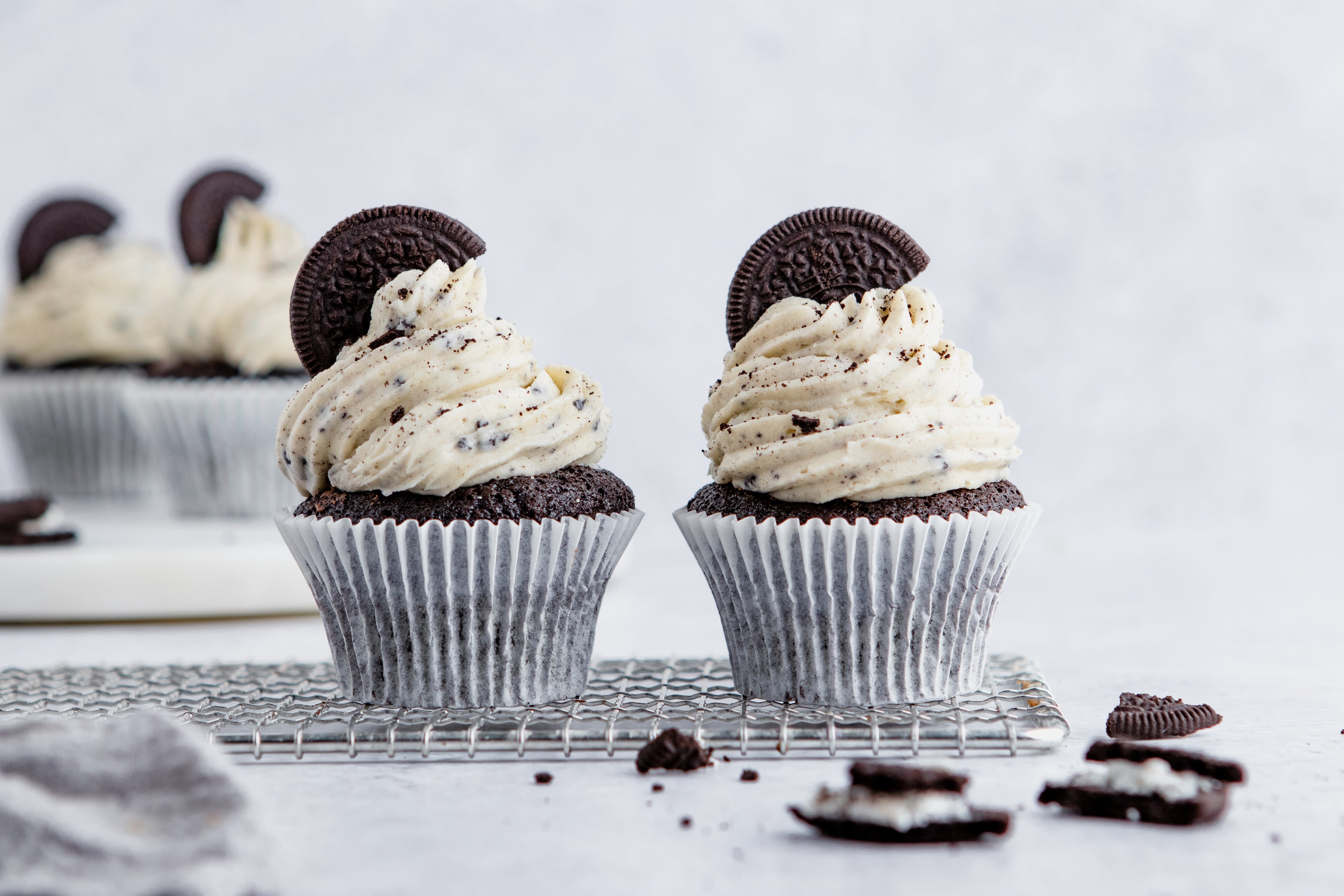 A pair of Oreo Cupcakes on a wire rack with oreo cookie crumbs