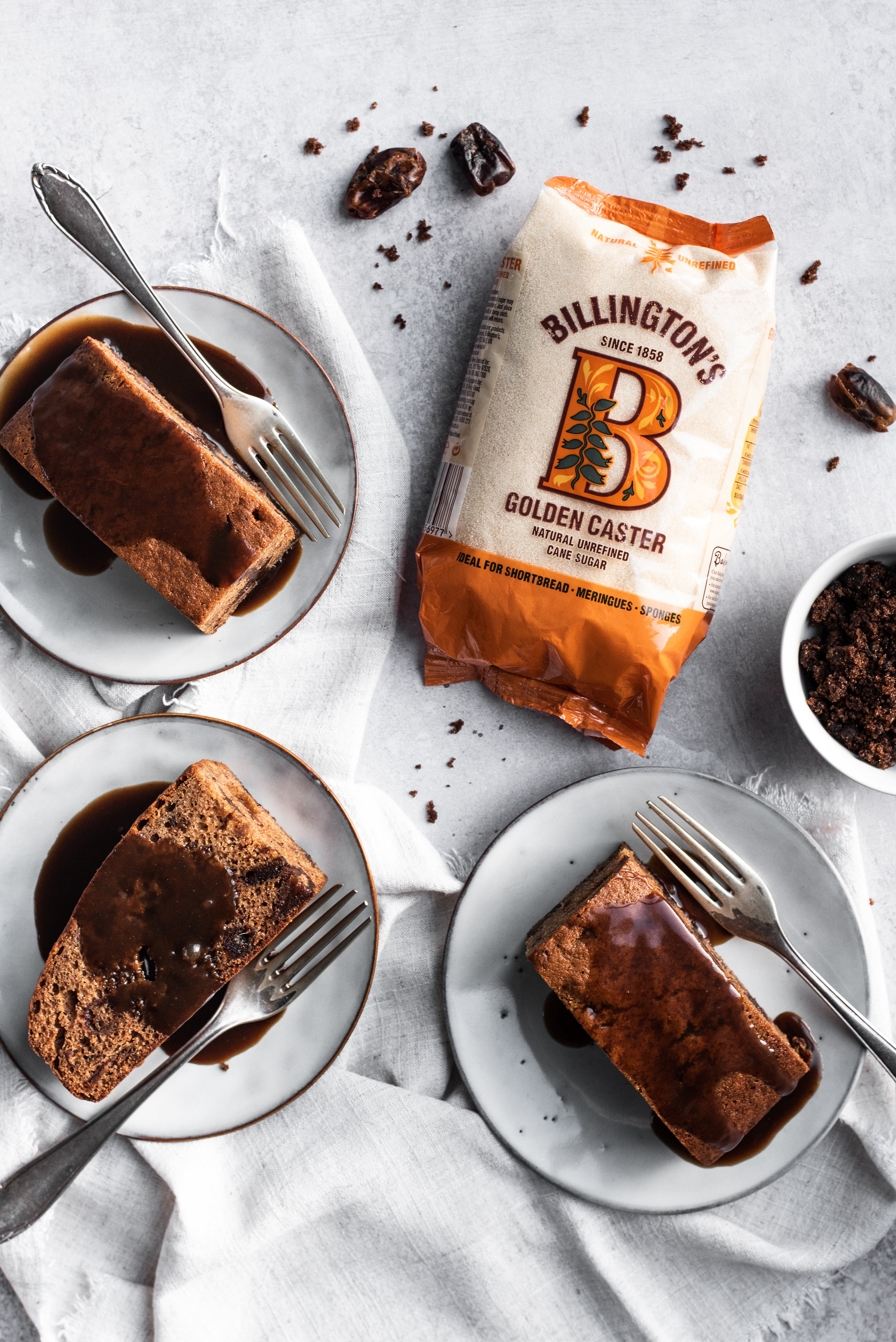 Three plates of sticky Toffee Pudding with a bag of golden caster sugar