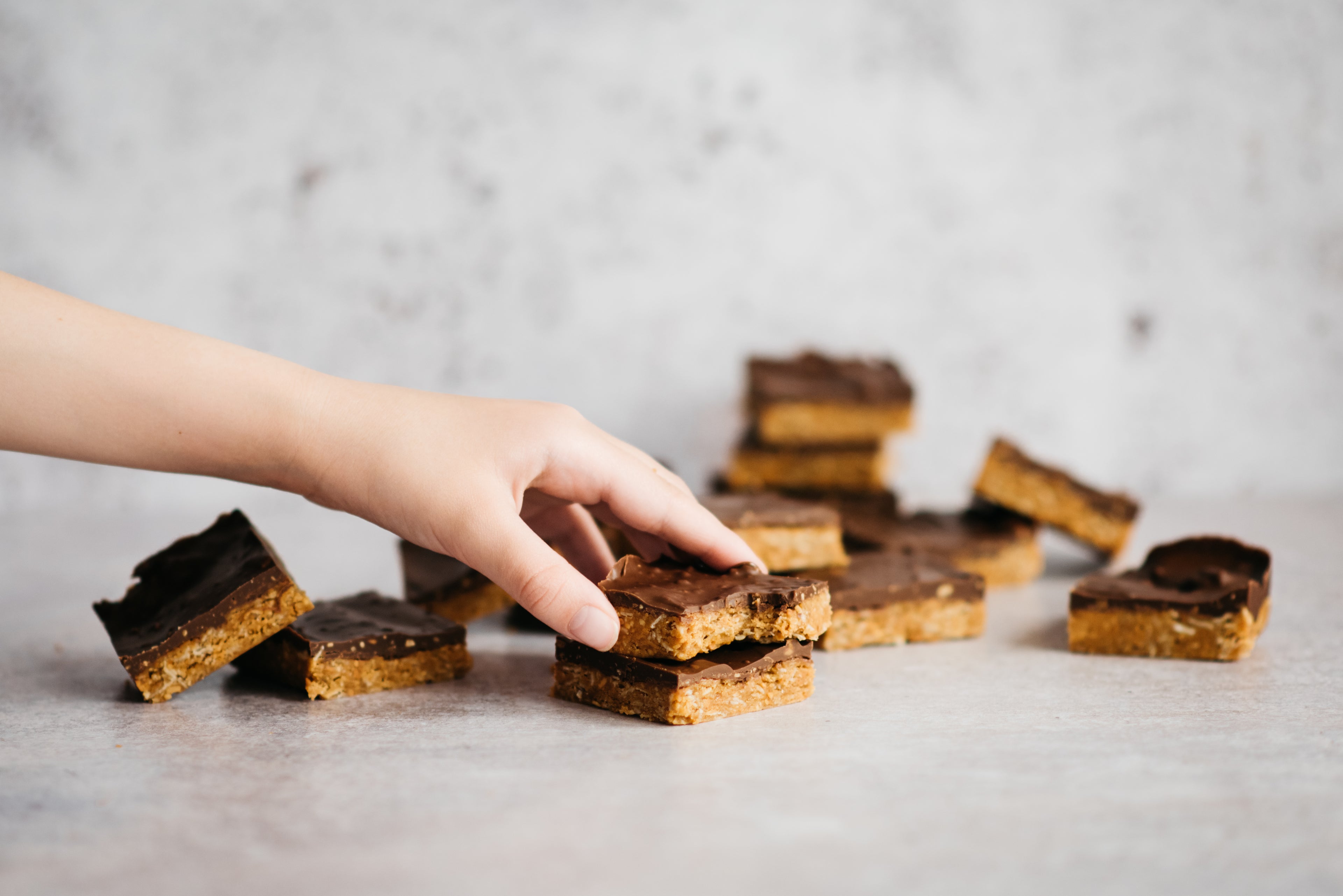 Hand reaching for a Chocolate Peanut Butter Square, with a batch cut up and stacked