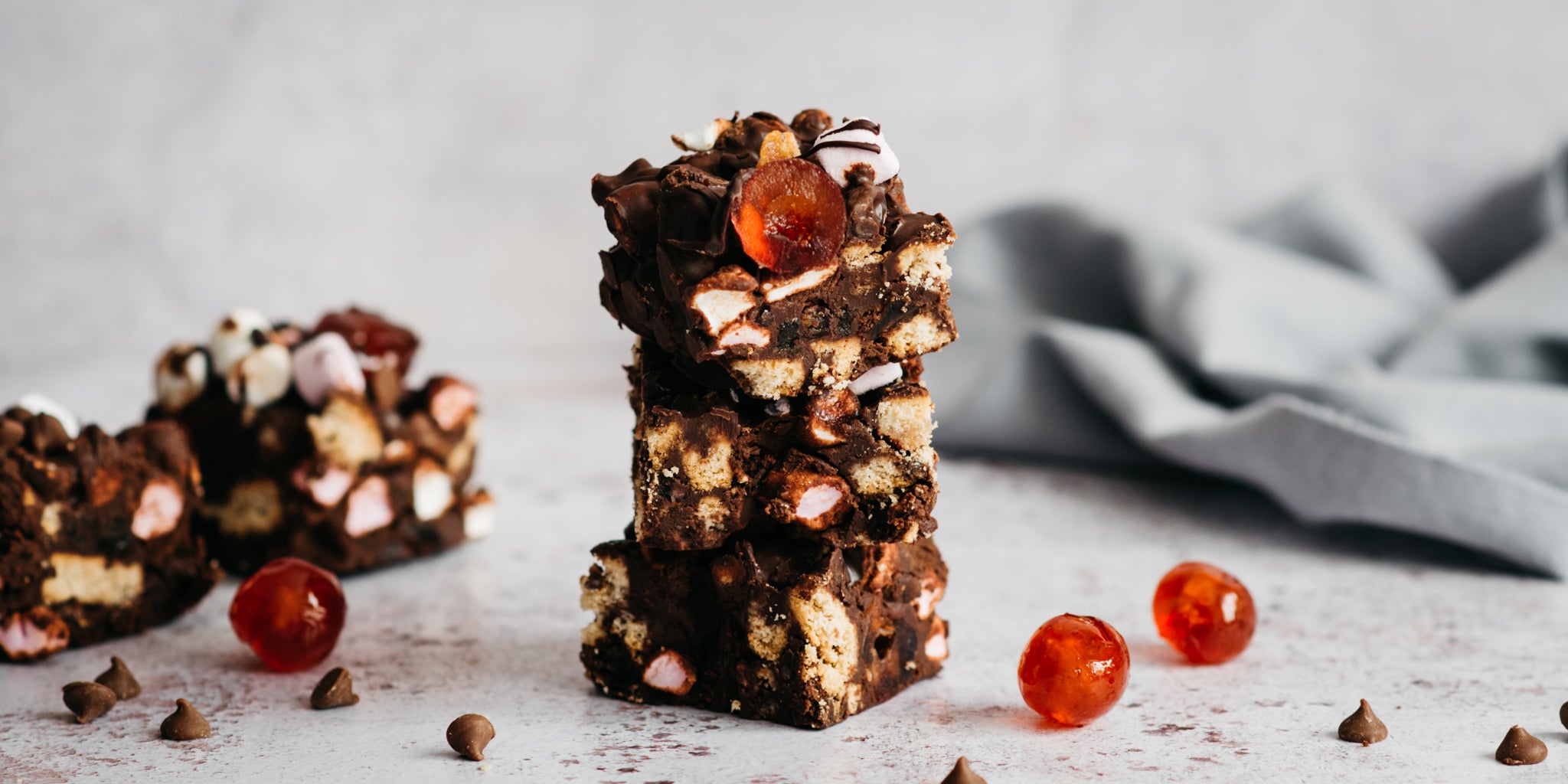 Close up of a stack of Vegan Rocky Road next to glace cherries and chocolate chips