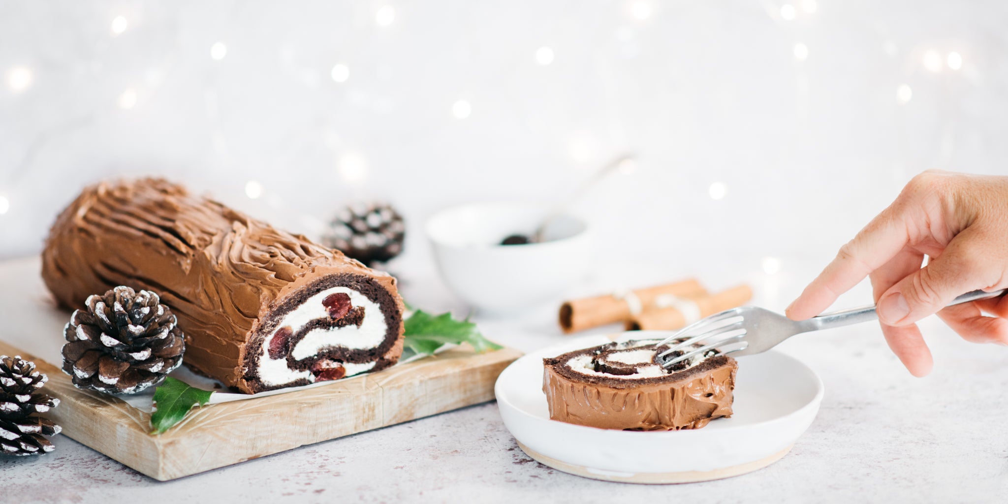 Black Forest Yule log on a wooden board with a slice on a plate in front and fork cutting into it