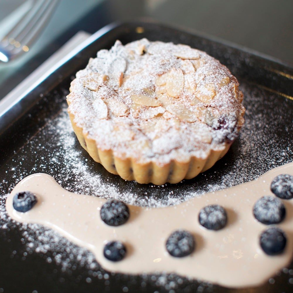 Blueberry tart made with a sweet Bakewell tart base, covered in icing sugar and flaked almonds