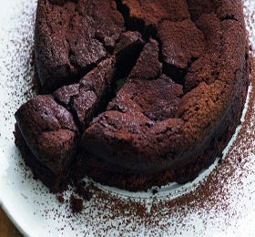 Chocolate torte with a slice cut out sitting on a white base