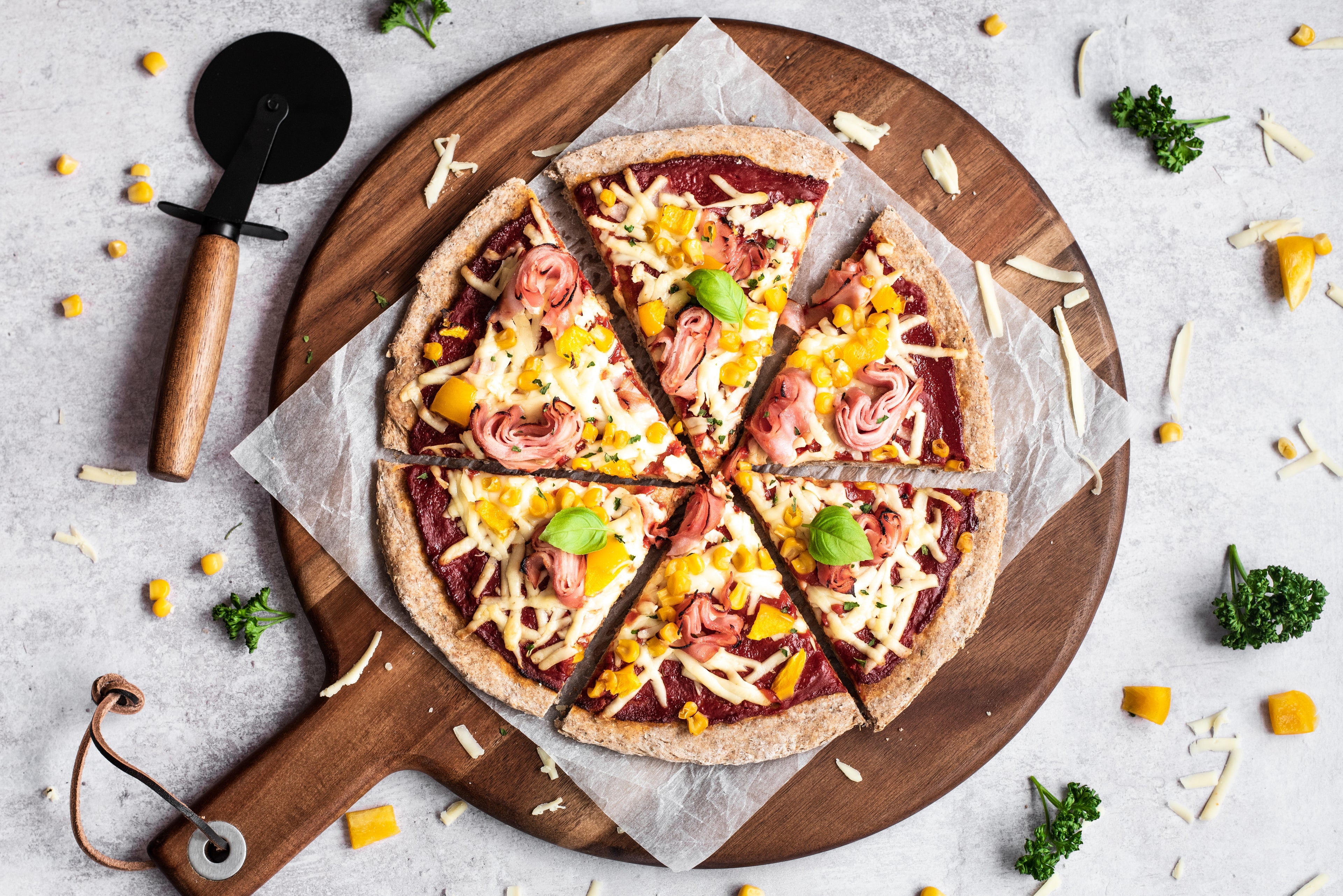 Overhead shot of pizza on chopping board with 6 slices cut and a pizza cutter