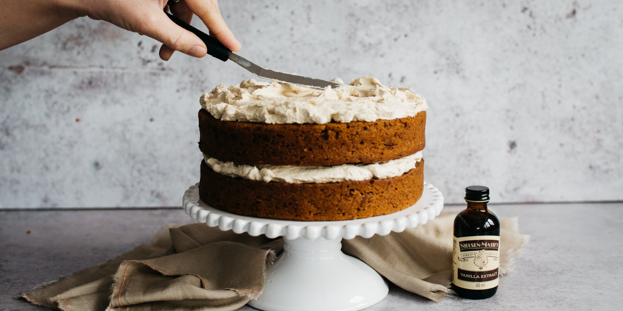 Vegan Carrot Cake being sliced into using a cake knife, next to a bottle of Nielsen-Massey vanilla extract