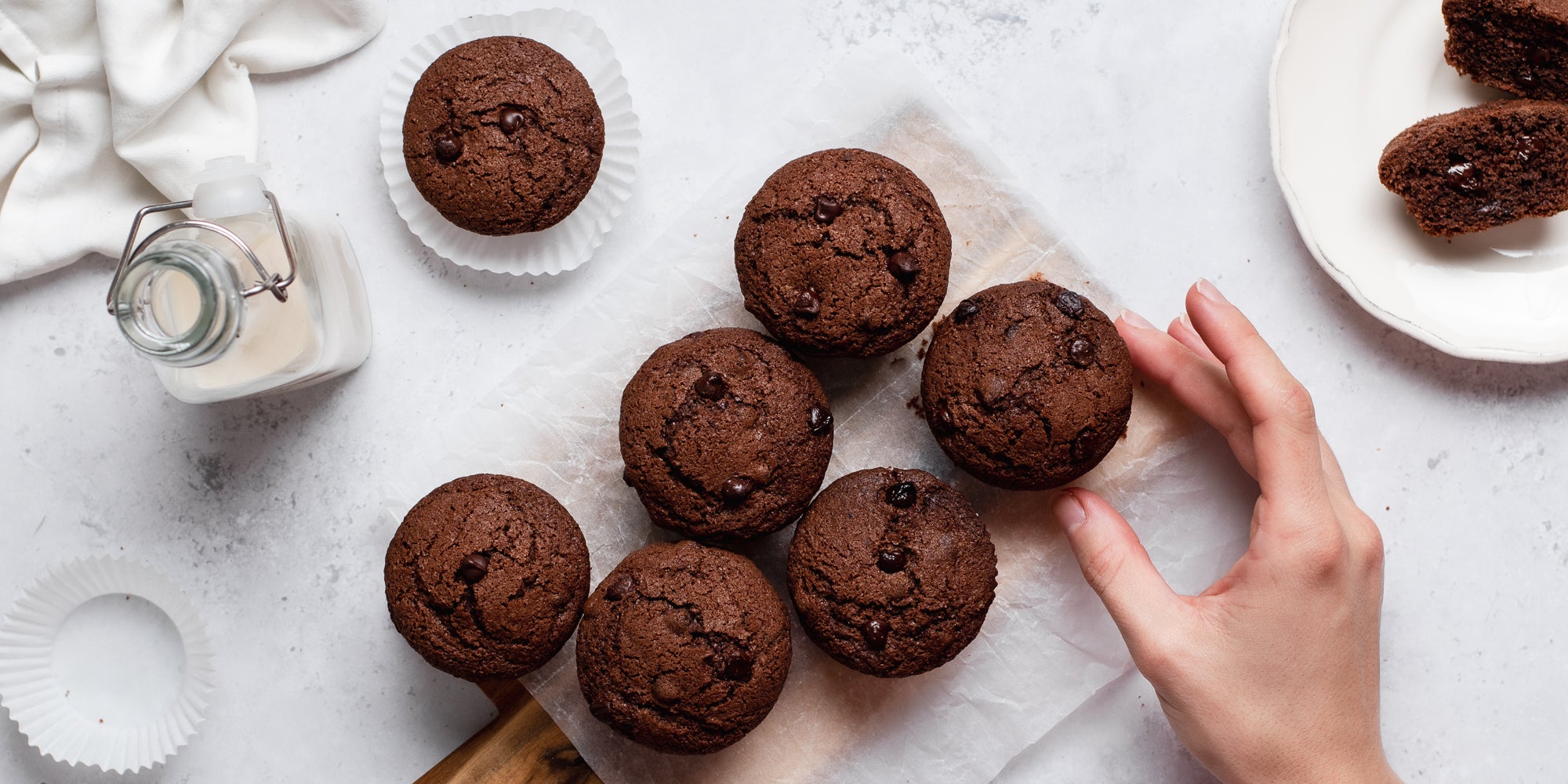 Gluten Free Chocolate Muffins with a hand reaching for a muffin next to a glass bottle of milk