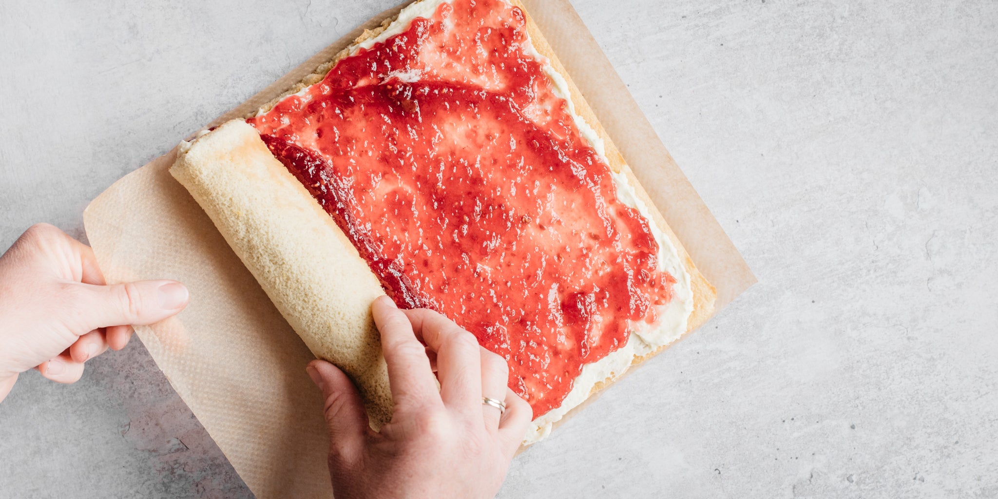 A top down view of a hand rolling up a vanilla swiss roll