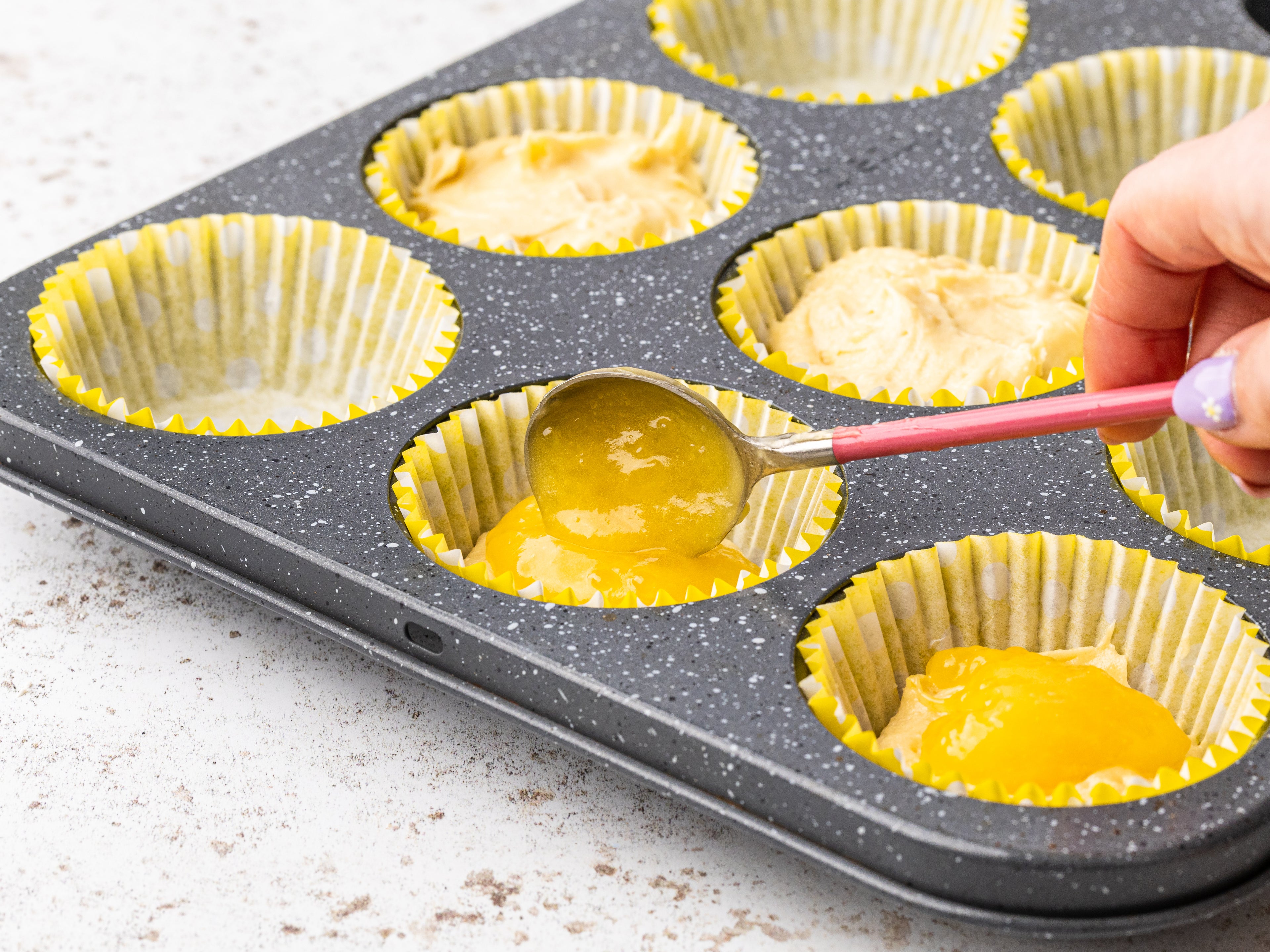 Lemon curd being spooned into cupcake cases on a baking tray