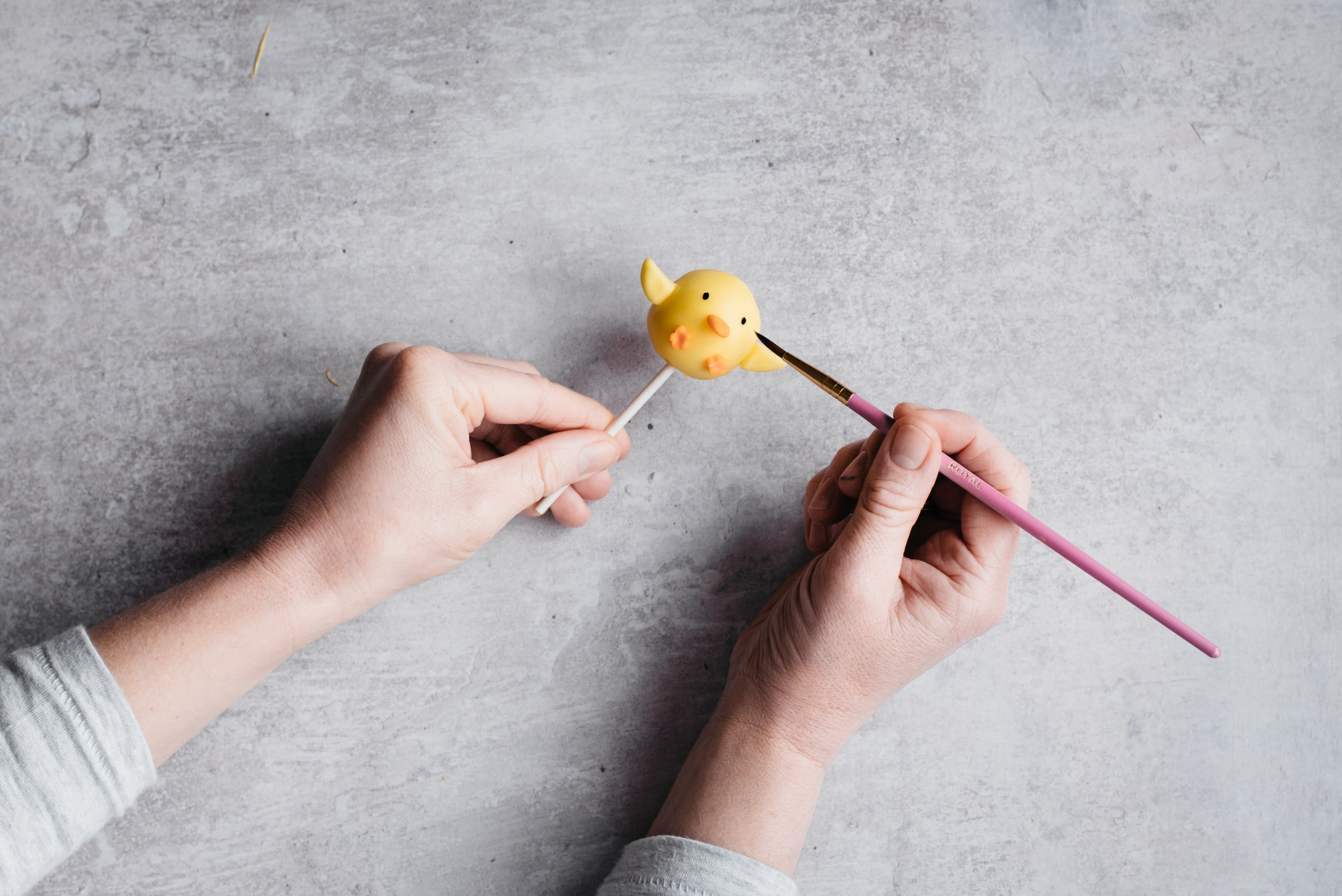 person holding cake pop drawing with black icing