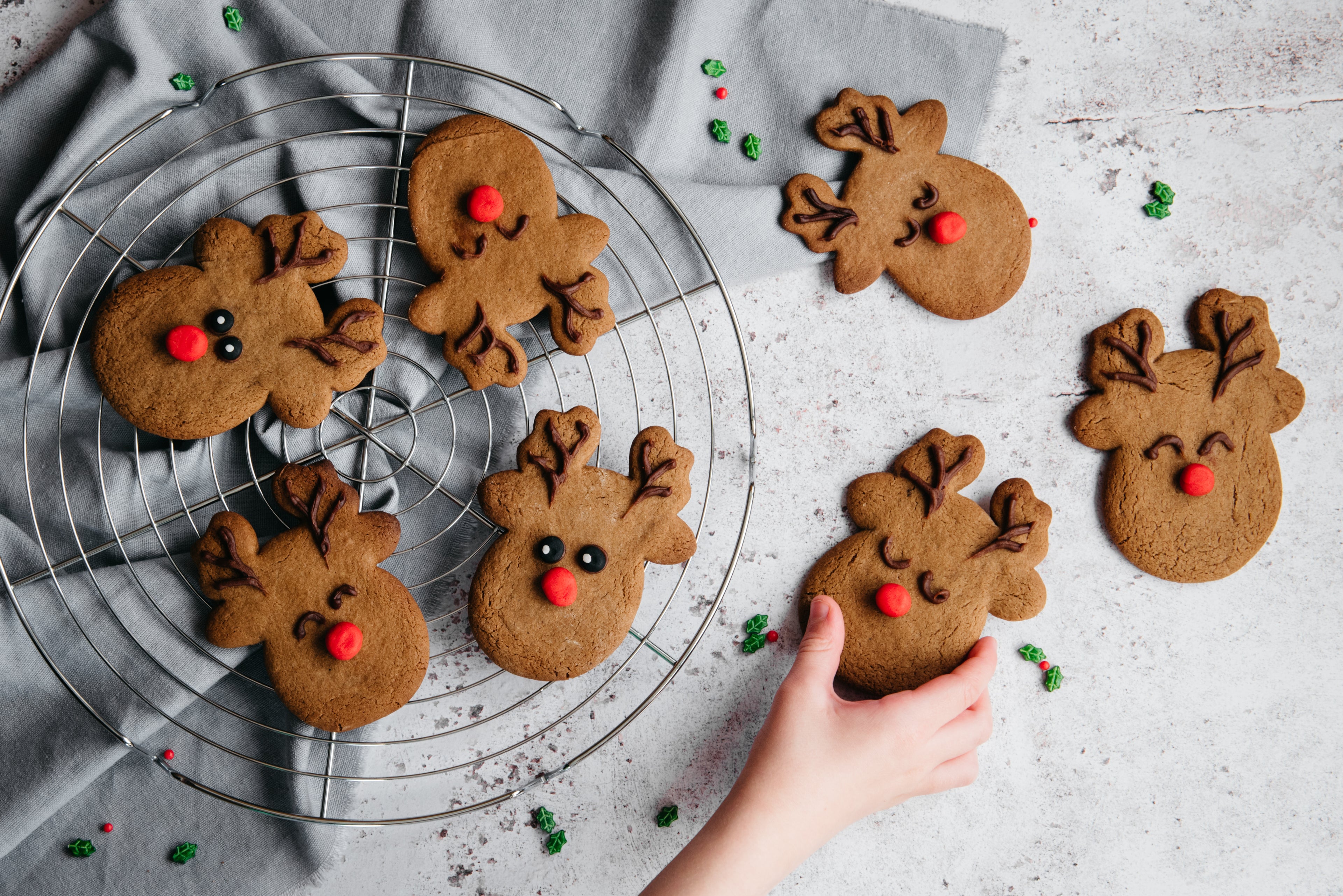 Top view of Reindeer Cookies on a wire rack, with a hand reaching for a cookie