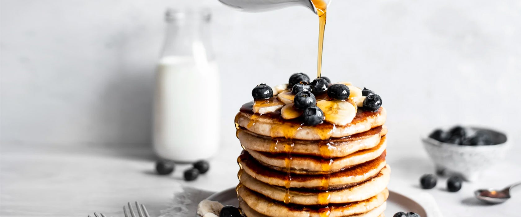 A stack of vegan pancakes with sliced banana and blueberries, drizzled with golden syrup