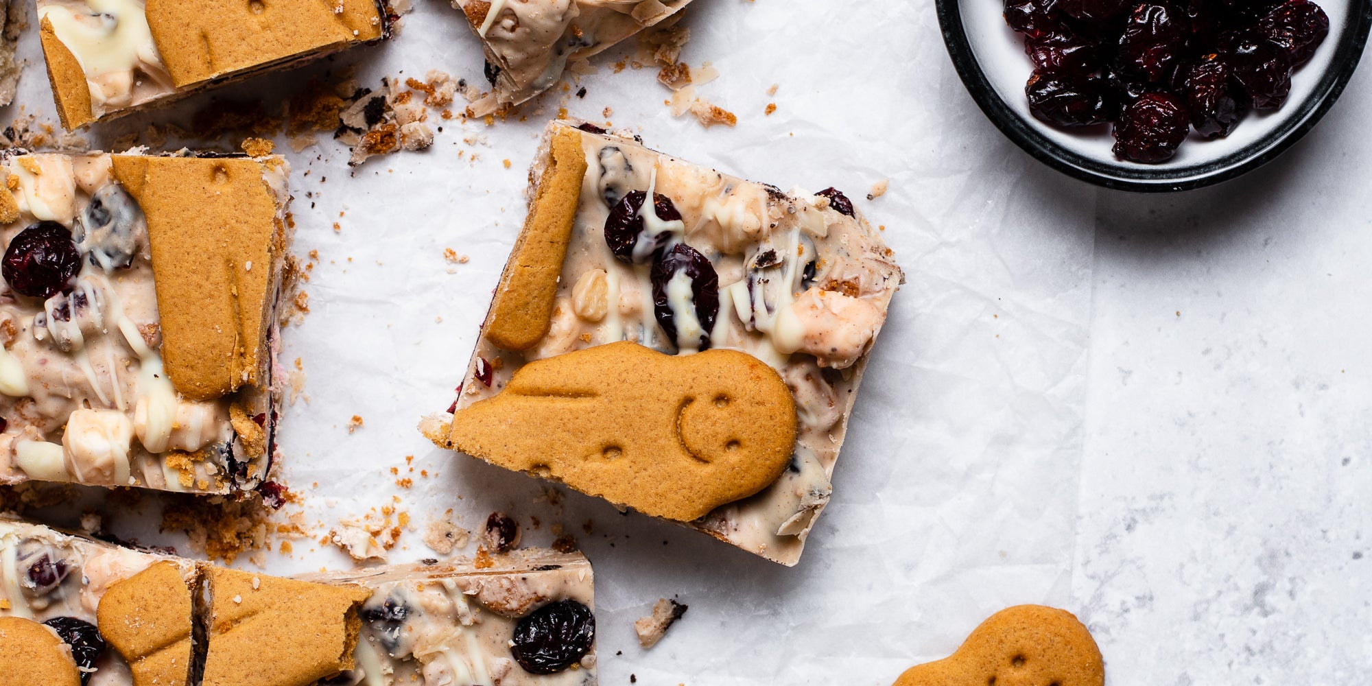 Close up of a square of White Chocolate & Cranberry Rocky Road with a gingerbread man on top, next to a bowl of cranberries