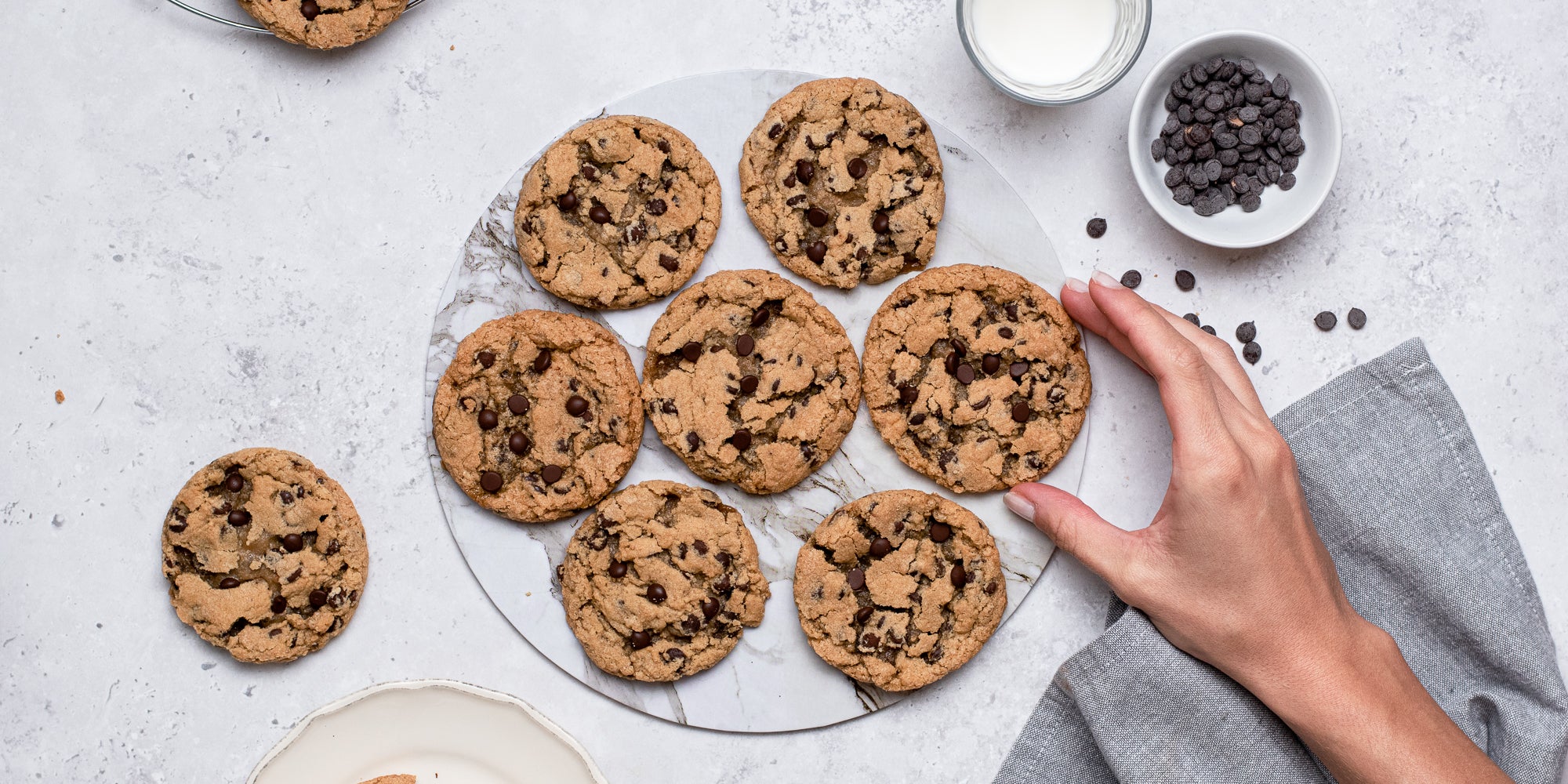 Top down view of a hand picking up a vegan and gluten free chocolate chip cookie from a plate