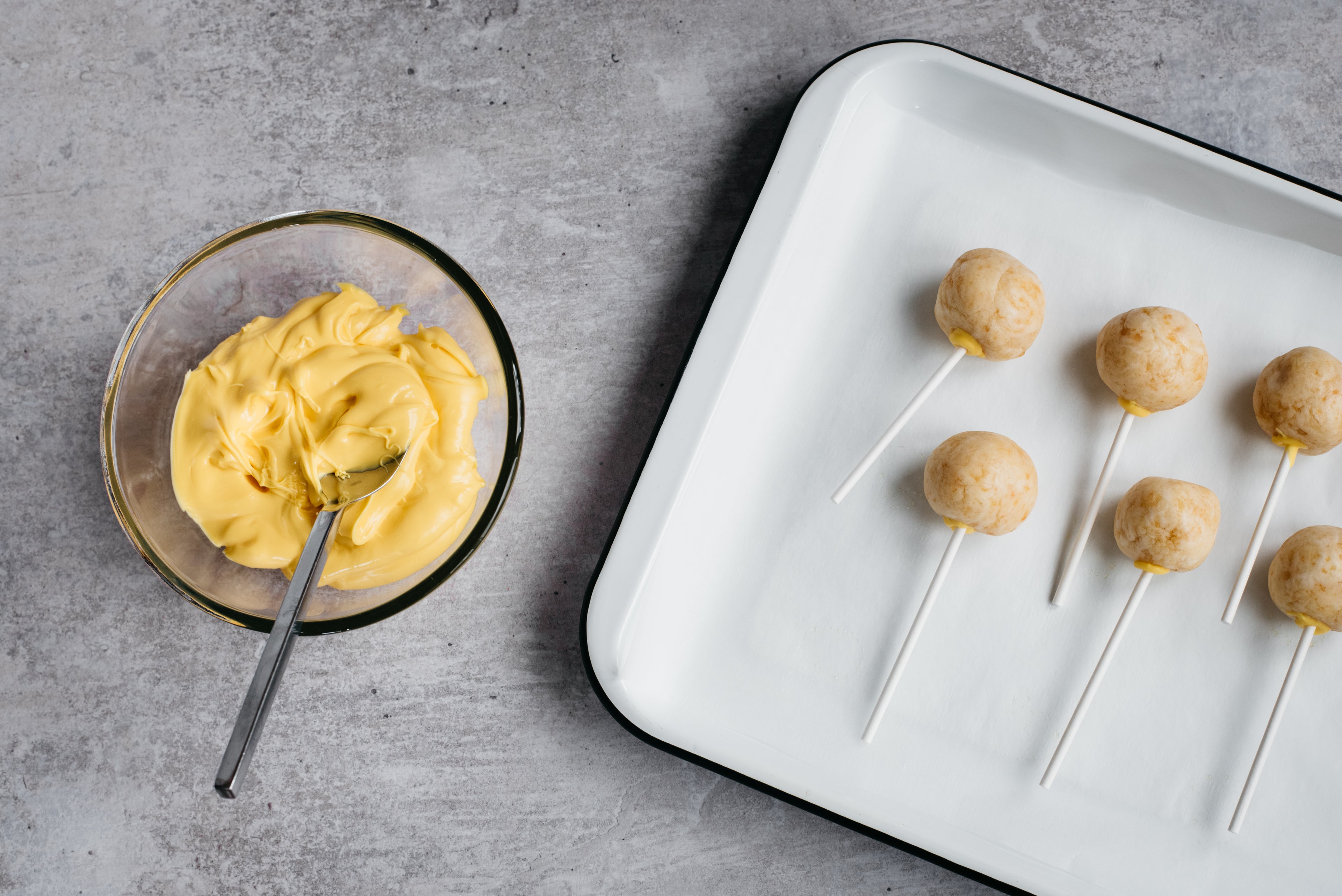 cake pops with lollipop sticks and a bowl of melted yellow chocolate on the left