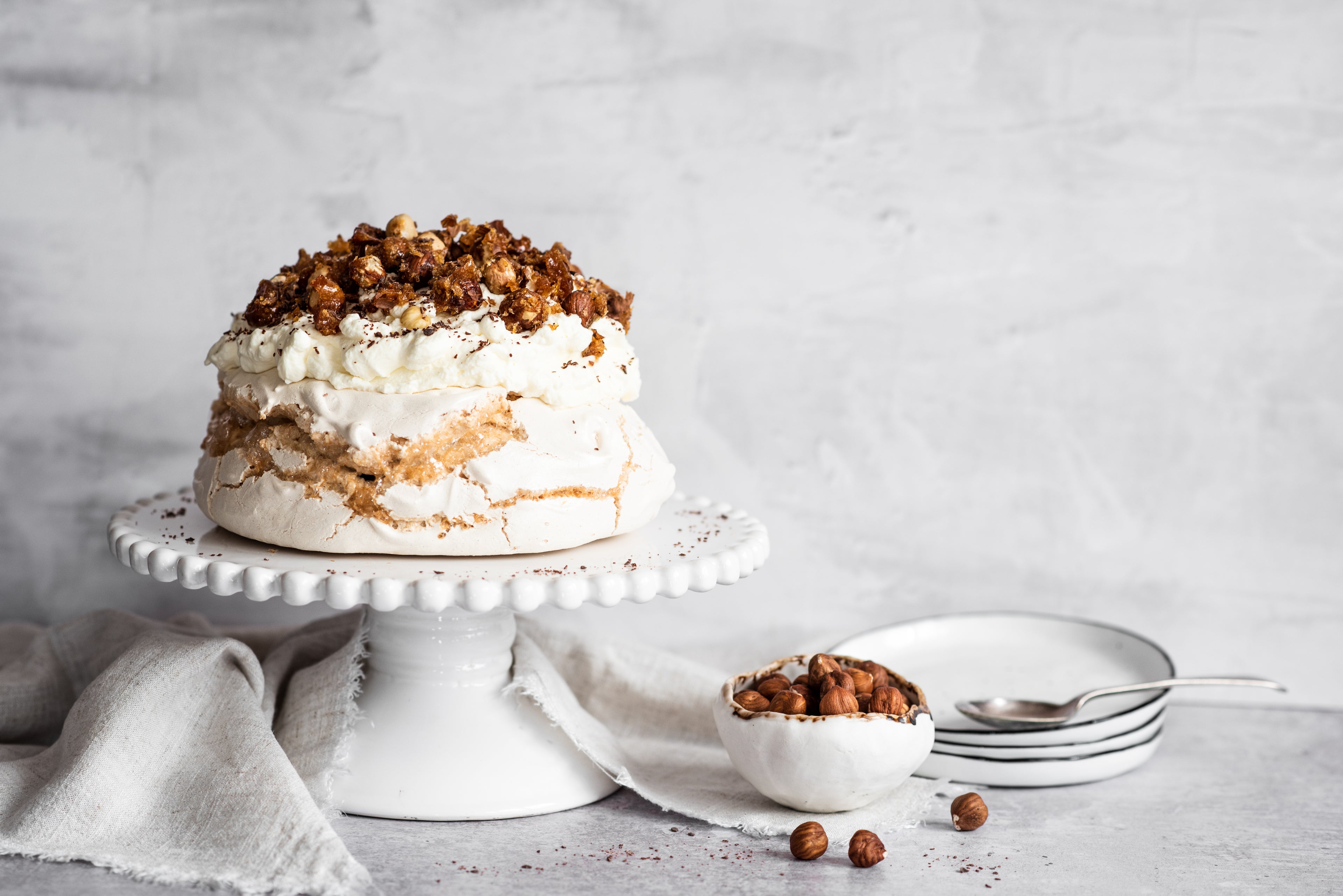 Coffee roasted hazelnut meringue on stand next to a bowl of hazelnuts