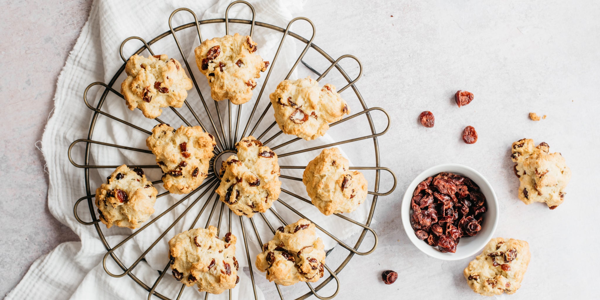 Rock buns on a circular cooling rack with a bowl of cranberries beside it