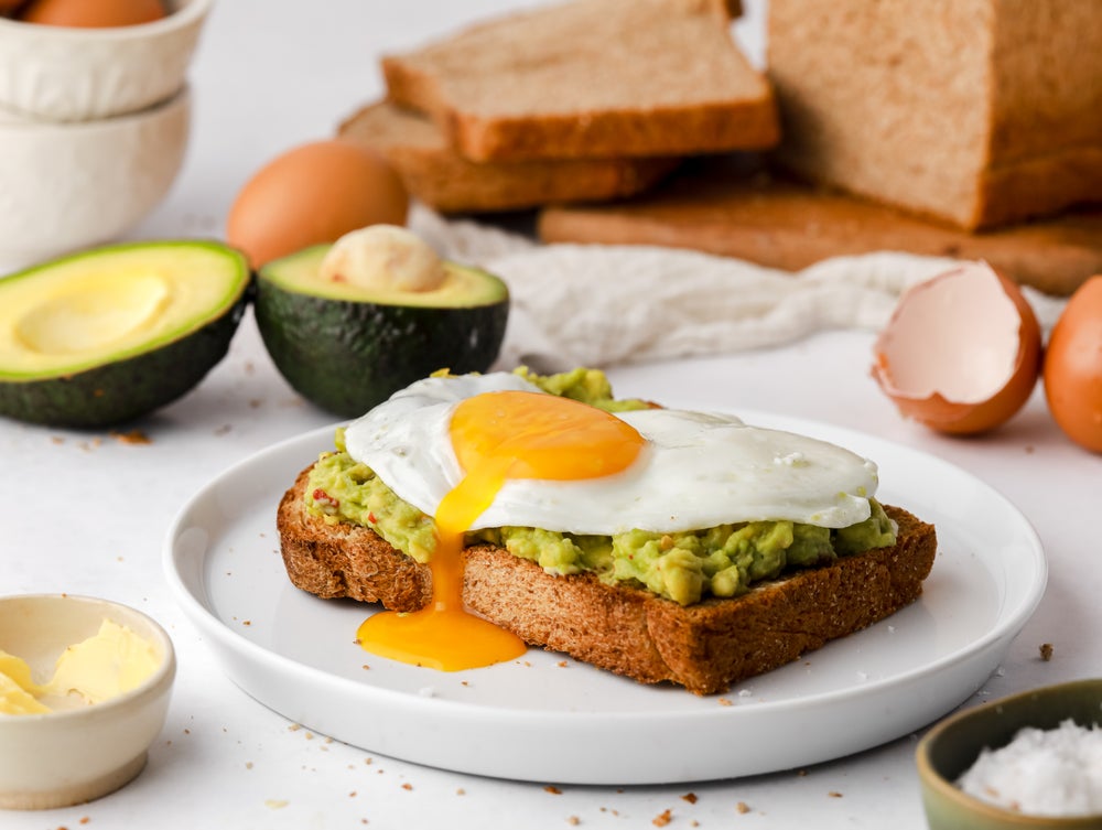 Avocado and egg on toast on a white plate. Chopped avocado in background