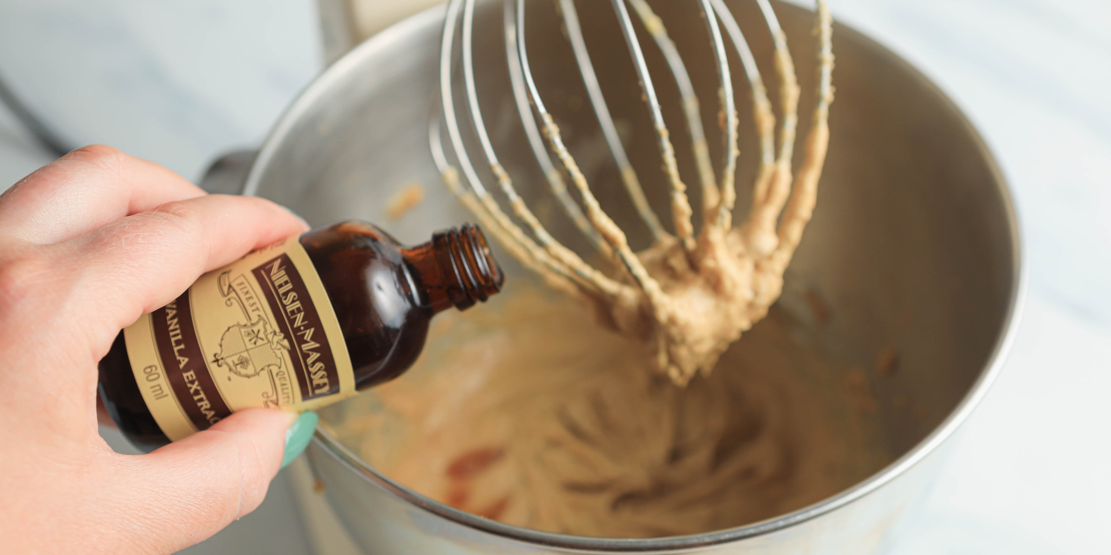 Hand pouring in vanilla extract to a cake mixer blending cookie mix