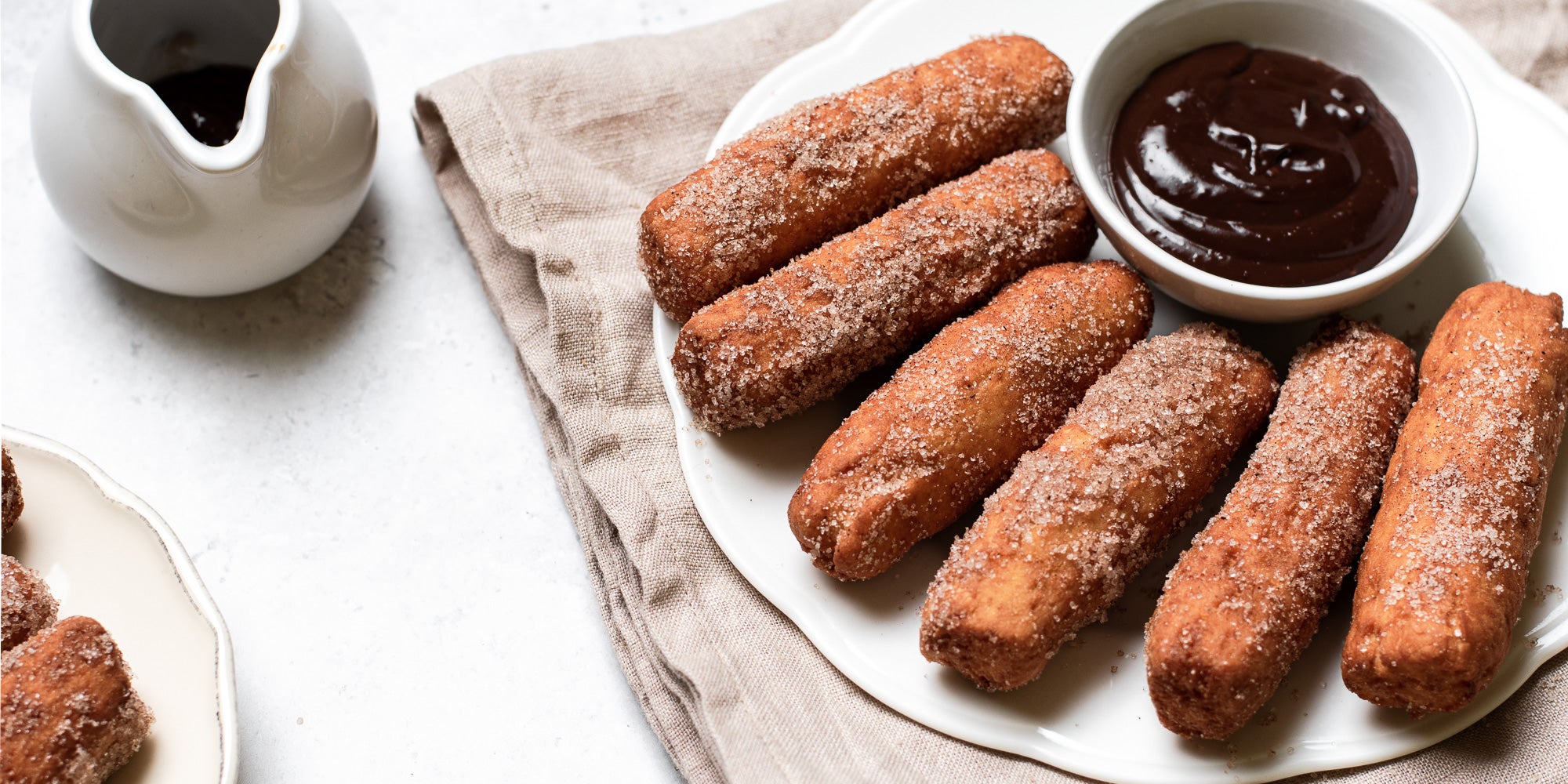 Doughnut Sticks with Chocolate Dip on a brown napkin, with a small jug of chocolate sauce