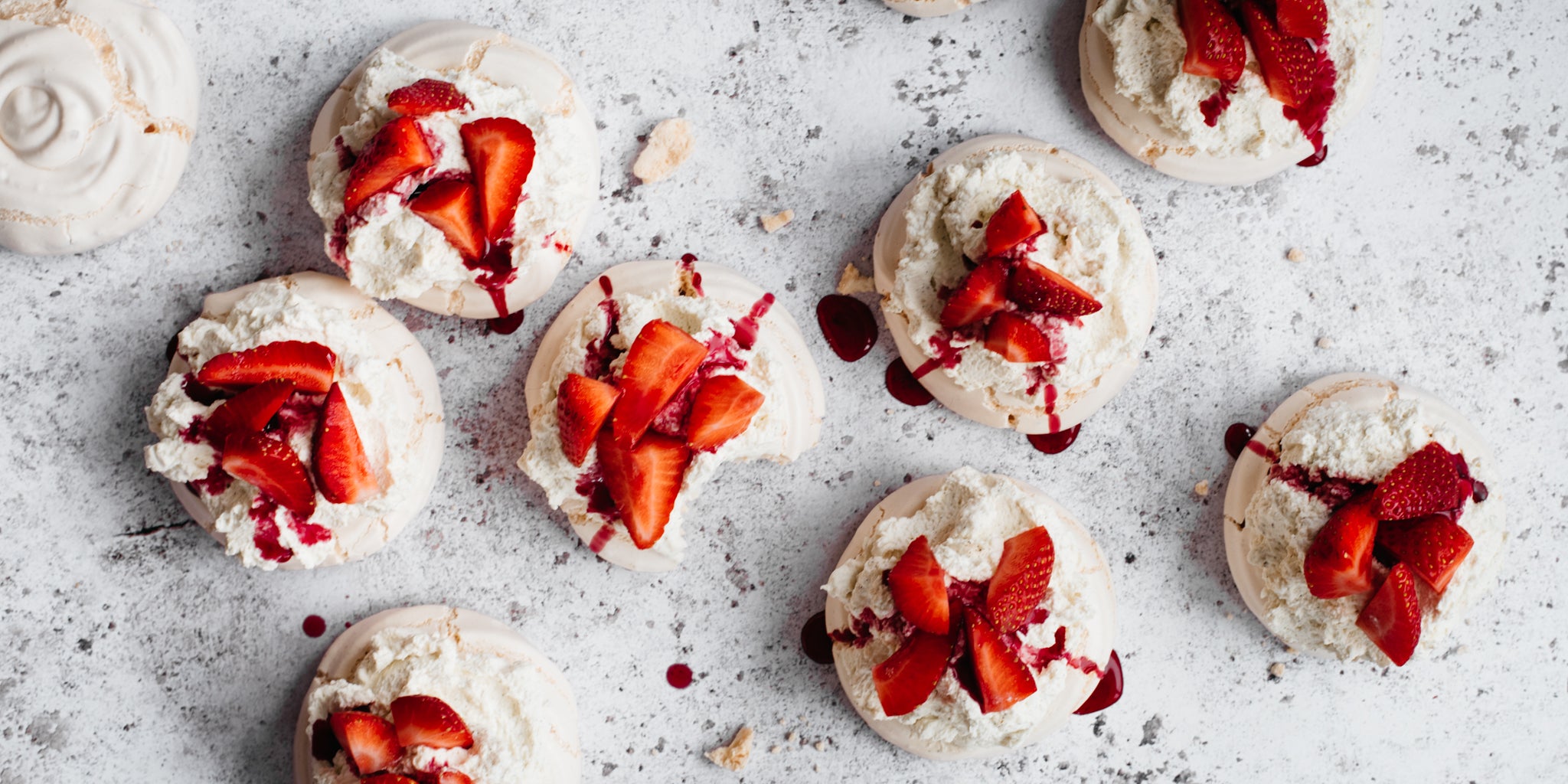Overhead shot of nine meringues topped with chopped strawberries, cream and strawberry sauce