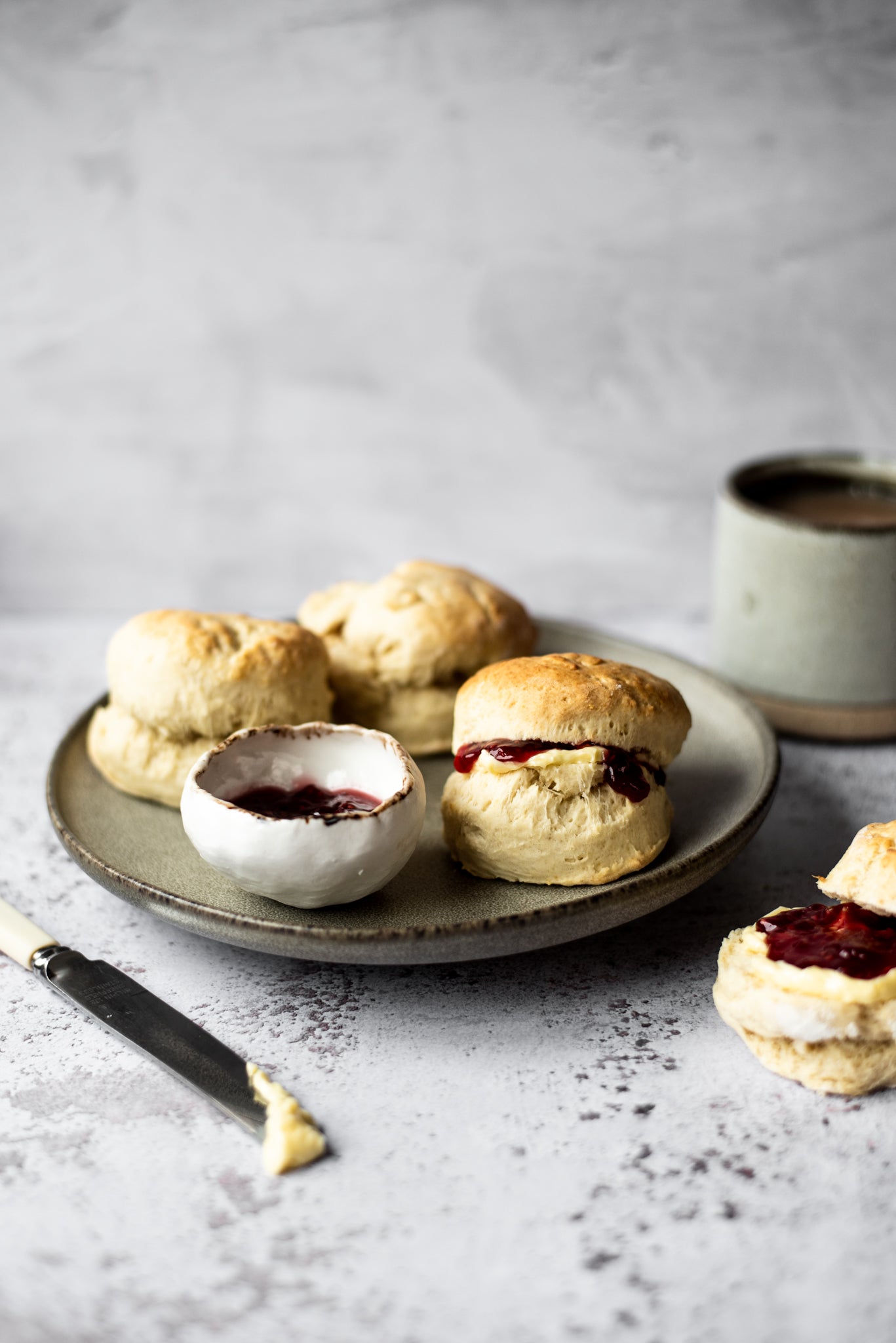 Three scones on a plate filled with jam and cream with pot of jam and knife with cream