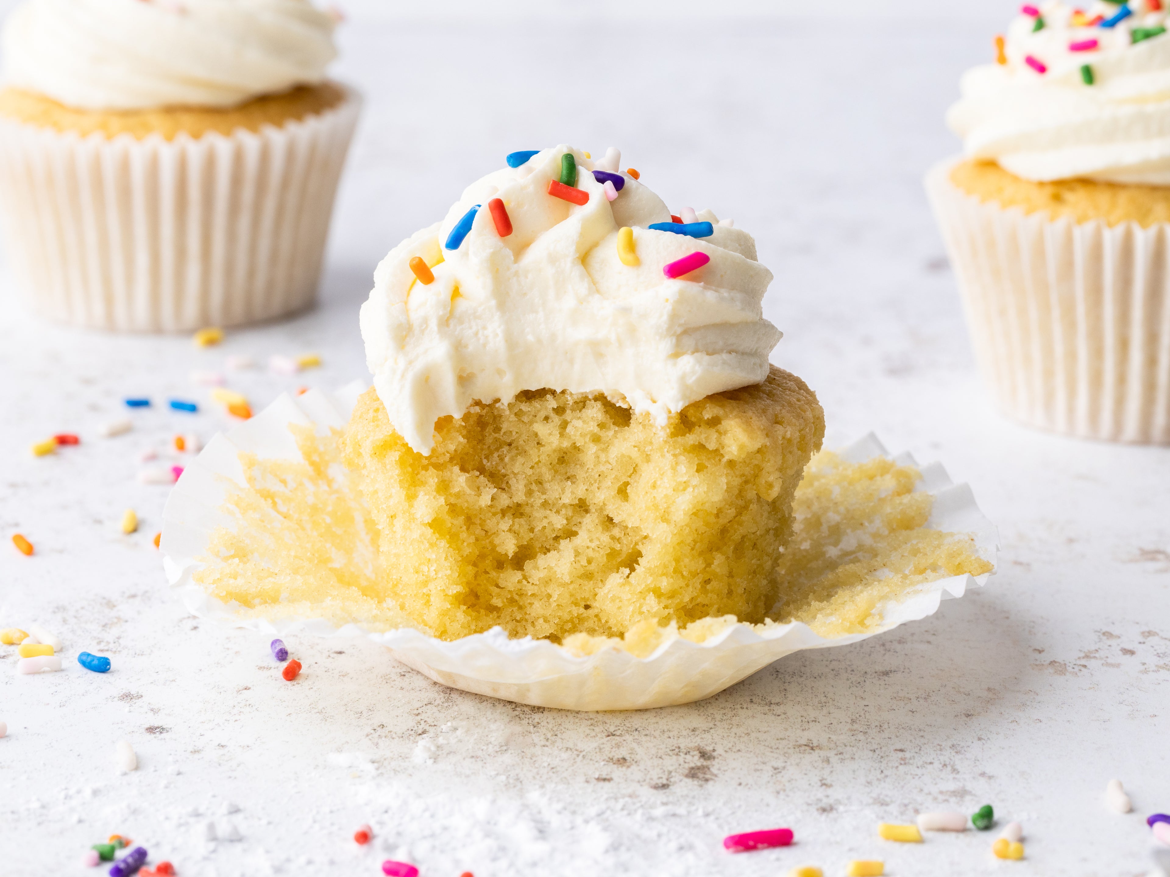Vanilla cupcakes with buttercream and sprinkles, with a bite taken out of it