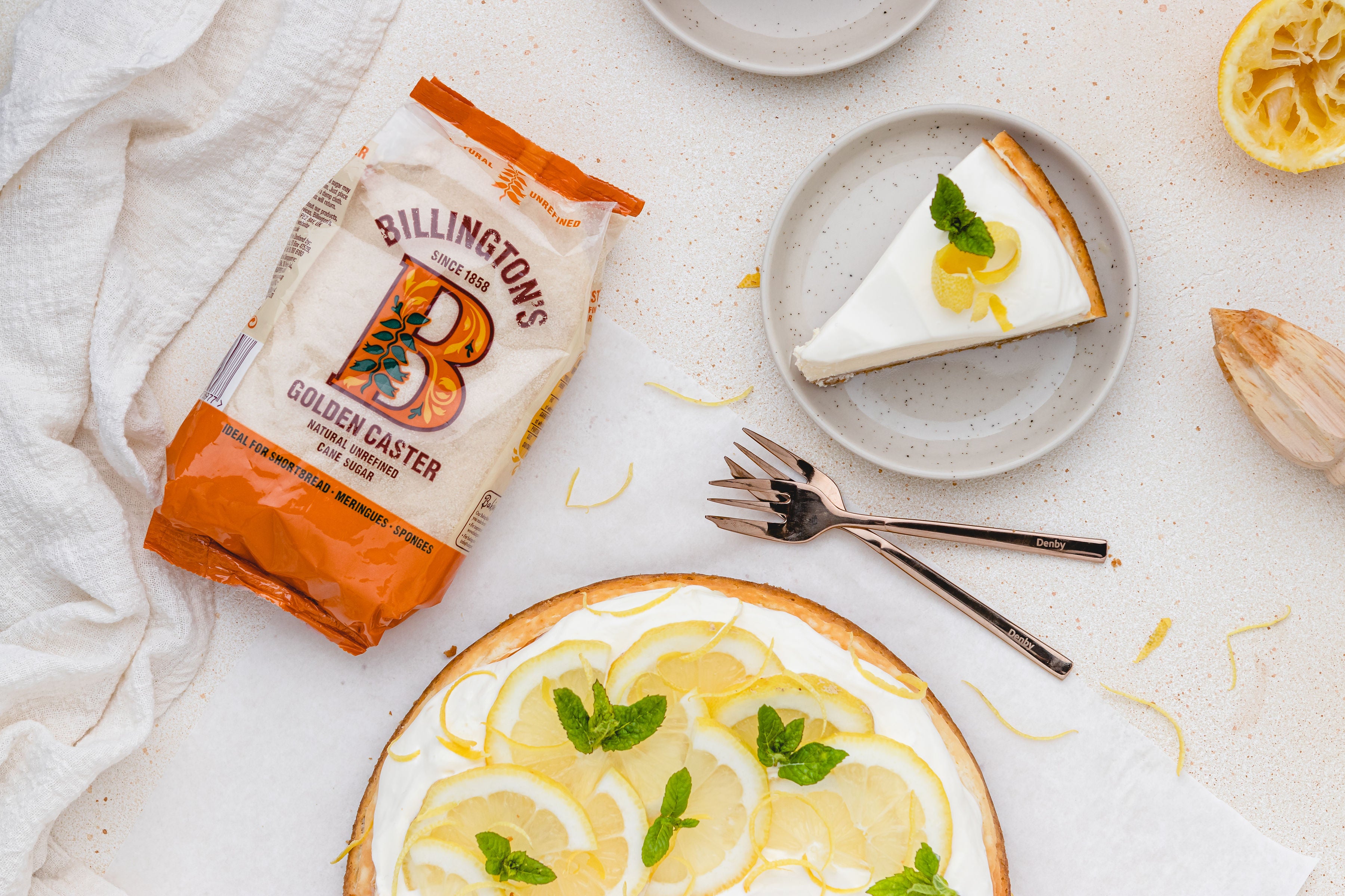 Slice of lemon cheesecake on plate, two forks and bag of sugar