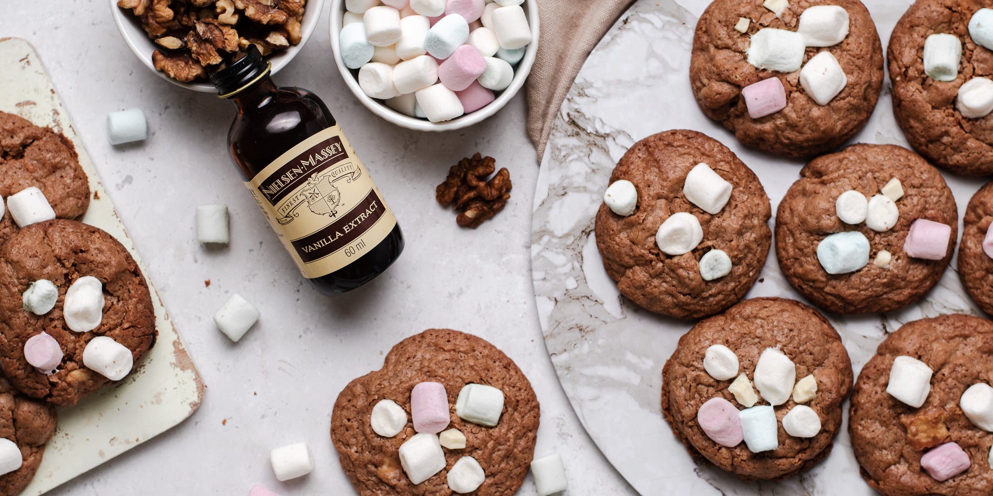 A batch of Rocky Road Cookies lay next to a bottle of Neilsen-Massey vanilla extract and a ramekin of mini marshmallows