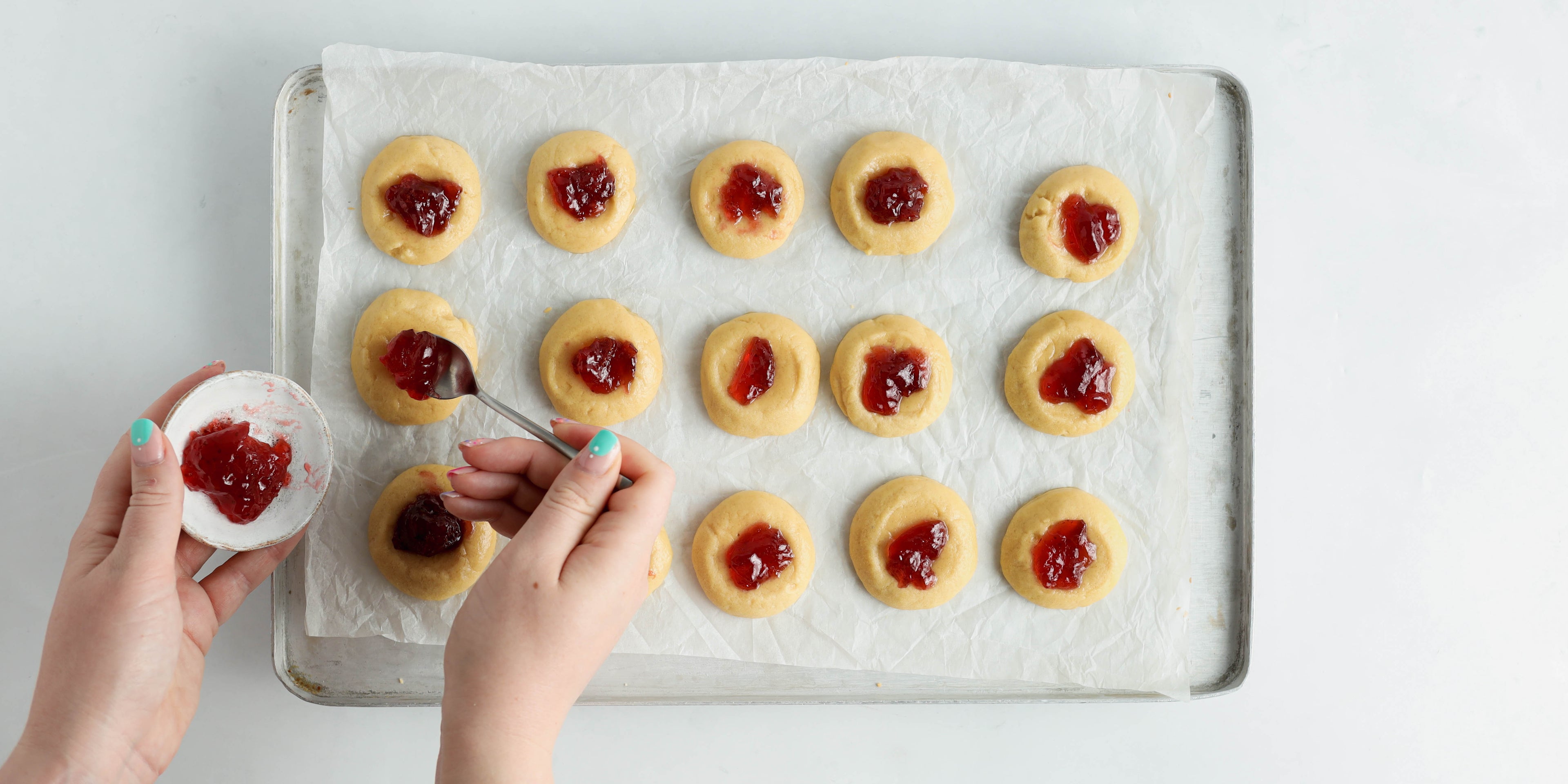 Tray of biscuits with a hand spooning jam on top with a spoon