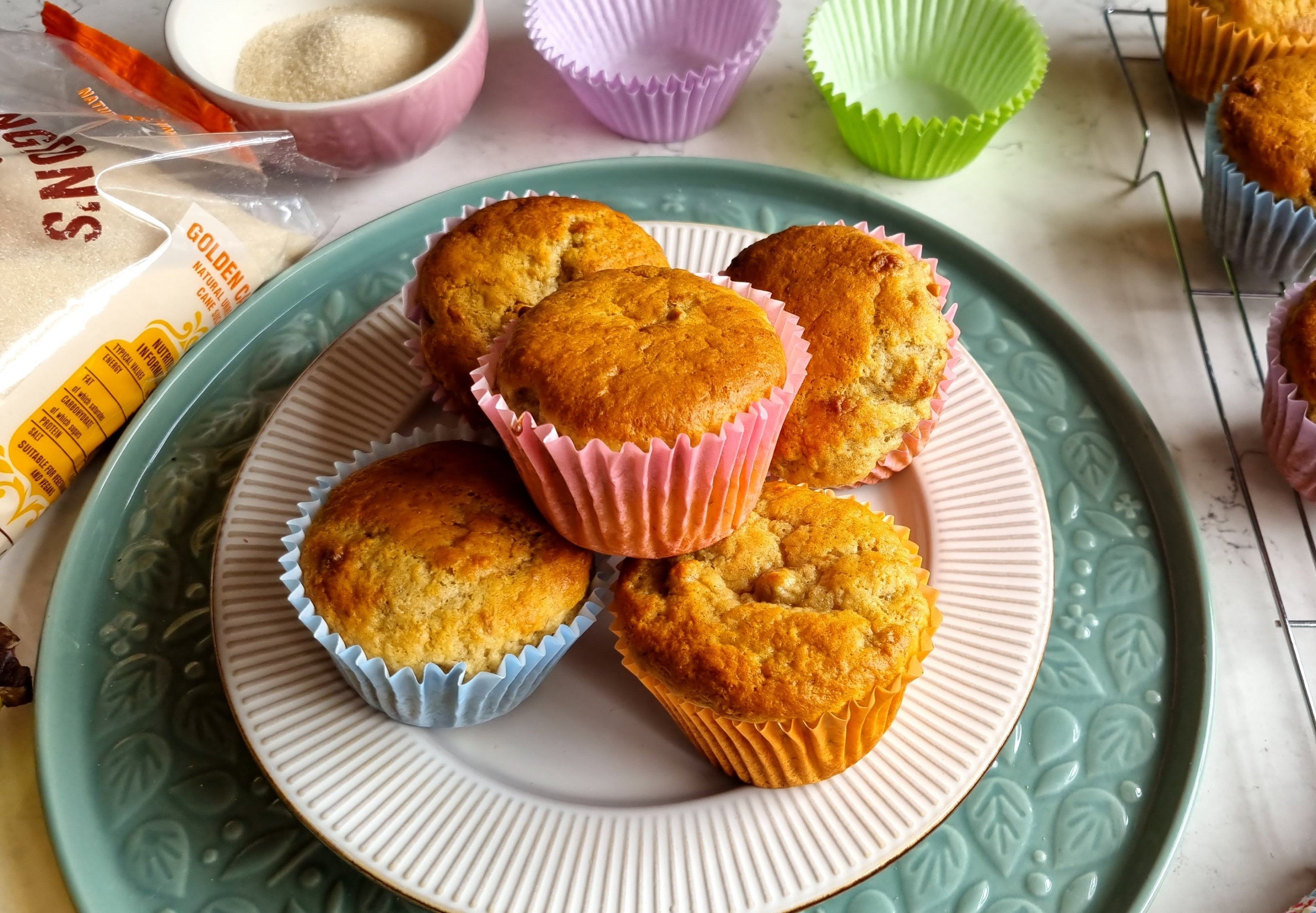 Plate of freshly-baked banana muffins with pastel-coloured cake cases