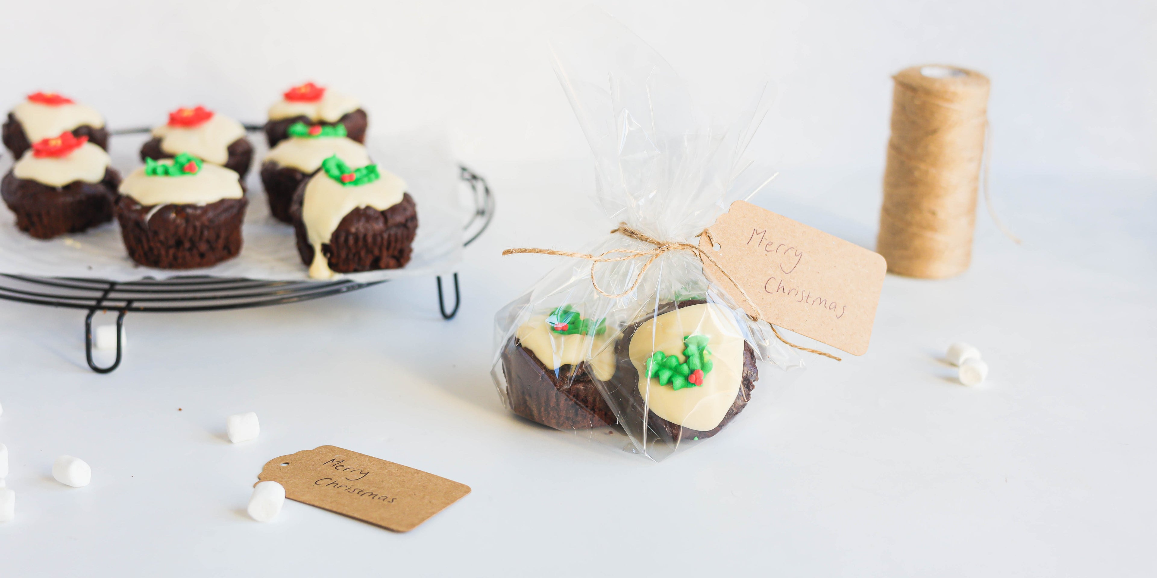 Mini Rocky Road Christmas Pudding Muffins on a wire rack, with a package of Mini Rocky Road Christmas Pudding Muffins hand tied in the foreground with a handwritten Christmas gift greeting