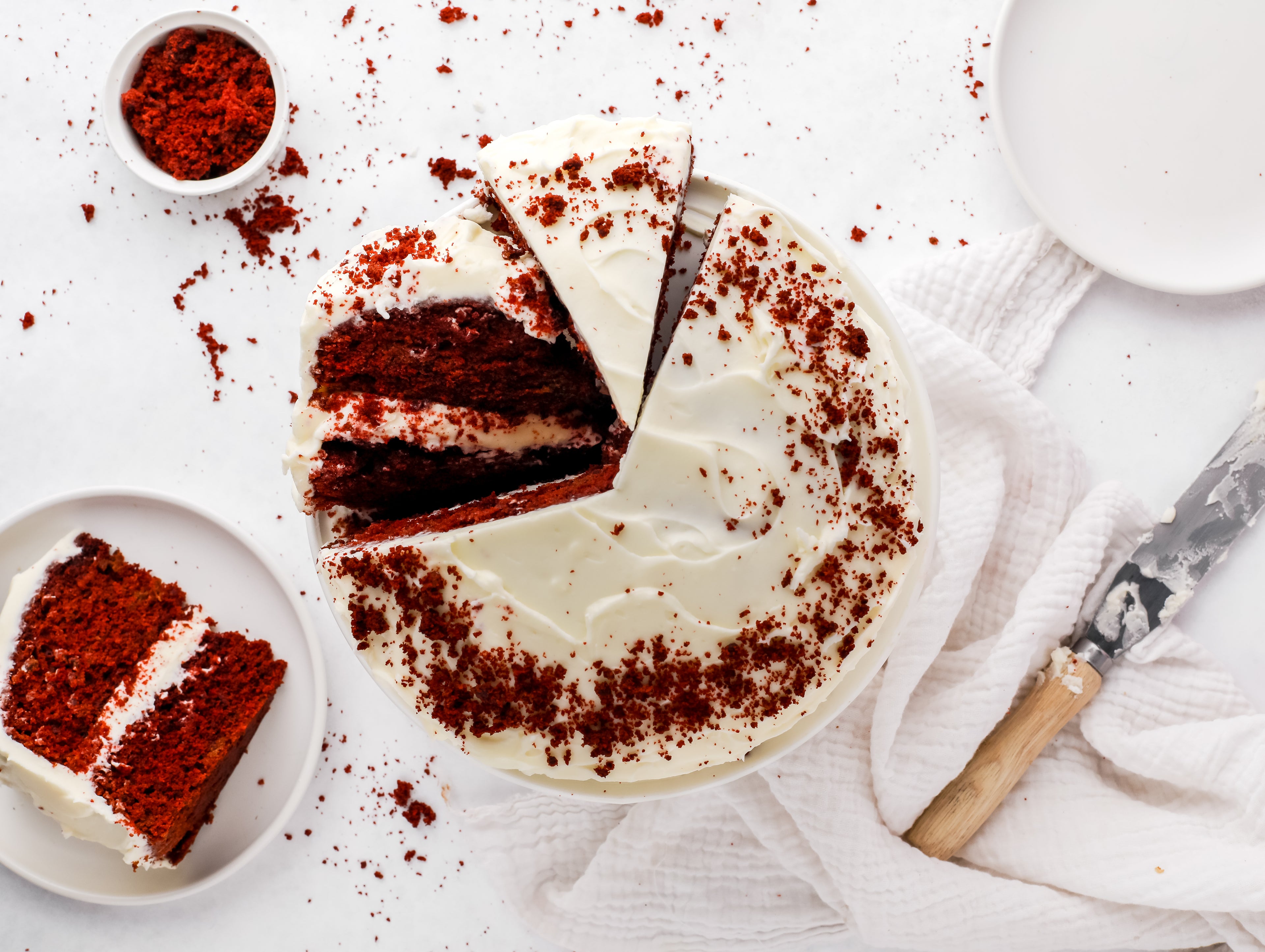 Top down shot of a sliced red velvet cake beside a cake knife and a slice on a plate
