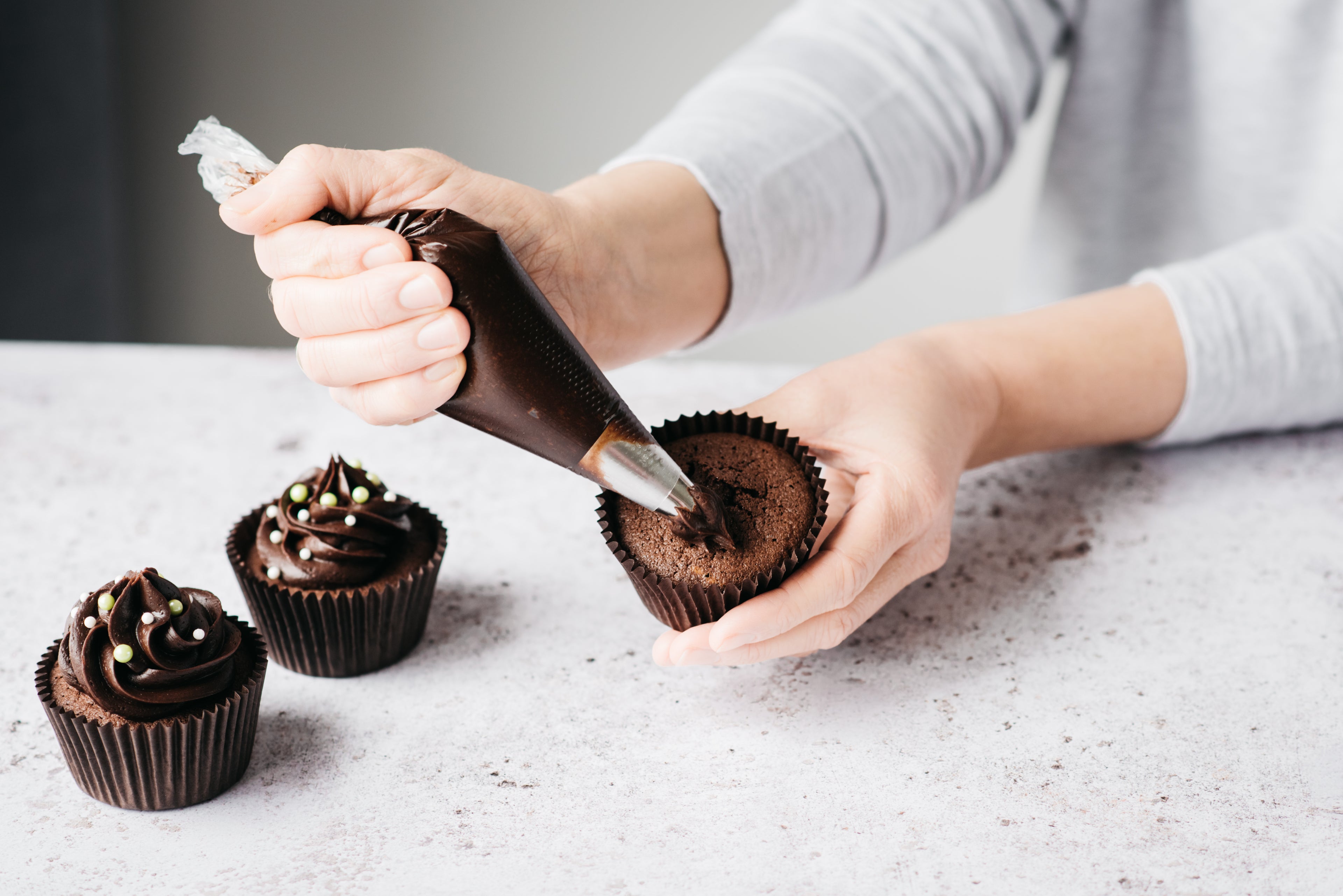 Chocolate buttercream being piped onto a chocolate cupcake
