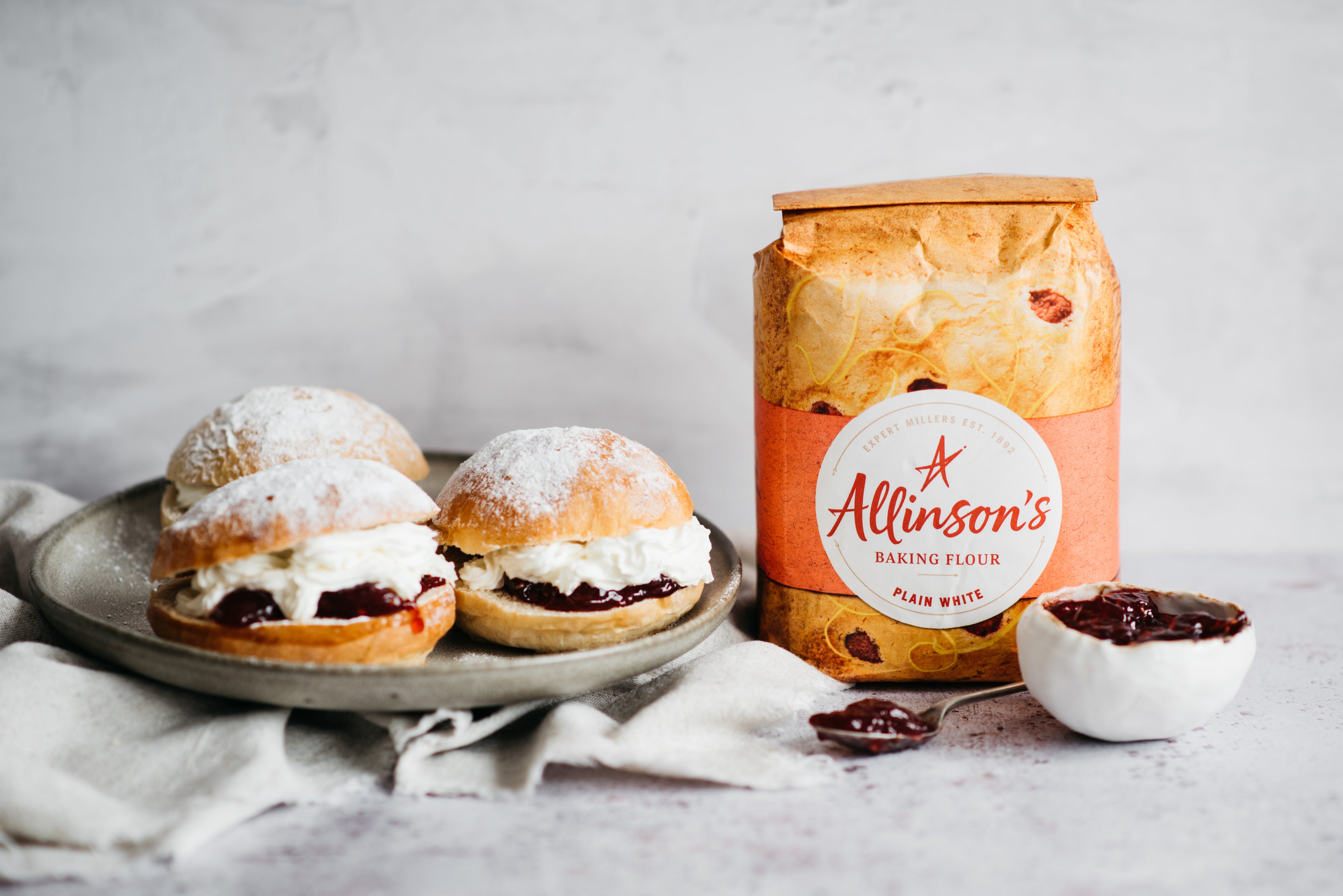 Plate of Devonshire Splits next to a bag of Allinson's plain white flour, with a bowl of jam and a spoon