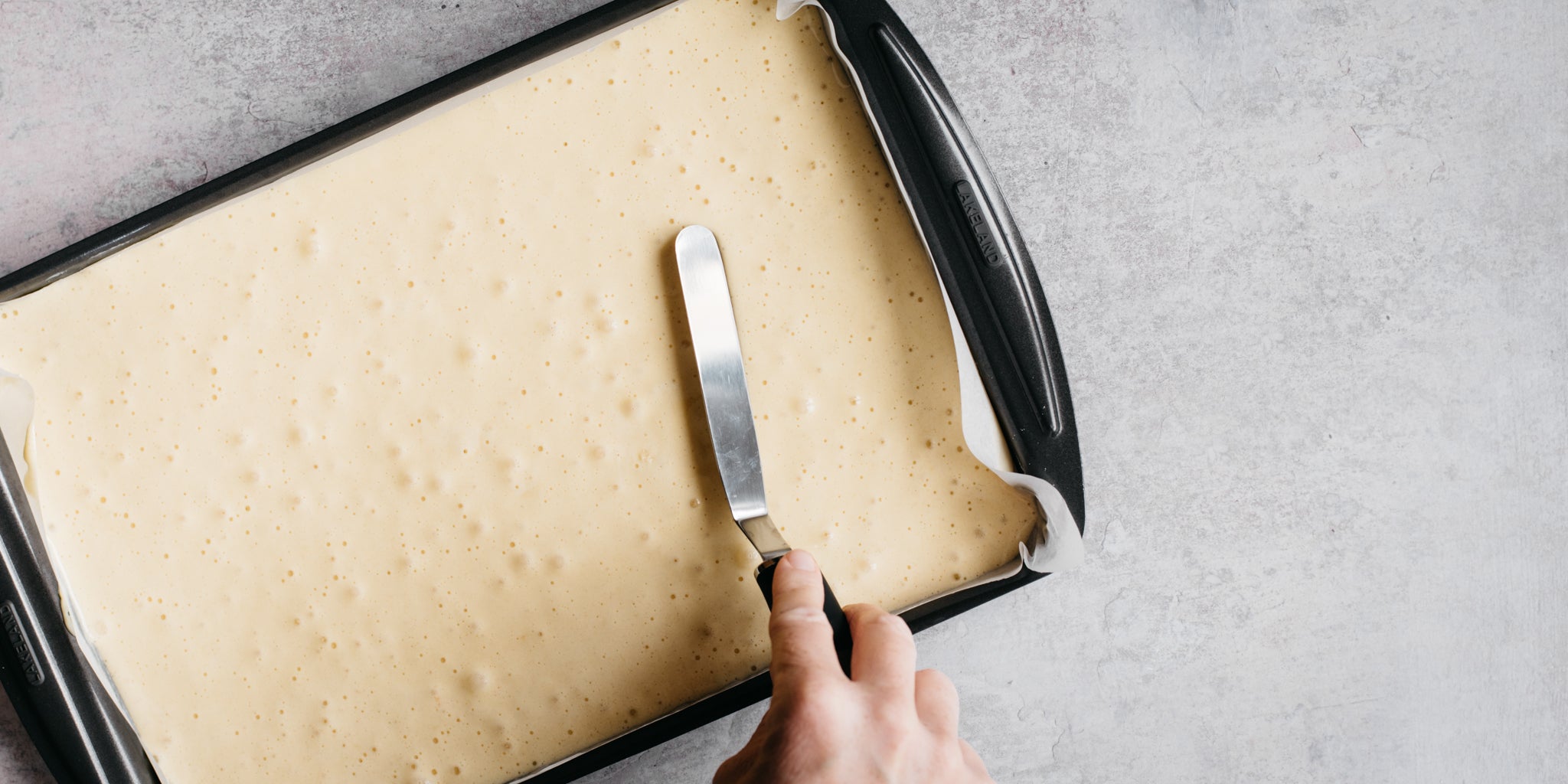 Pallet knife spreading out cake mixture in flat baking tin