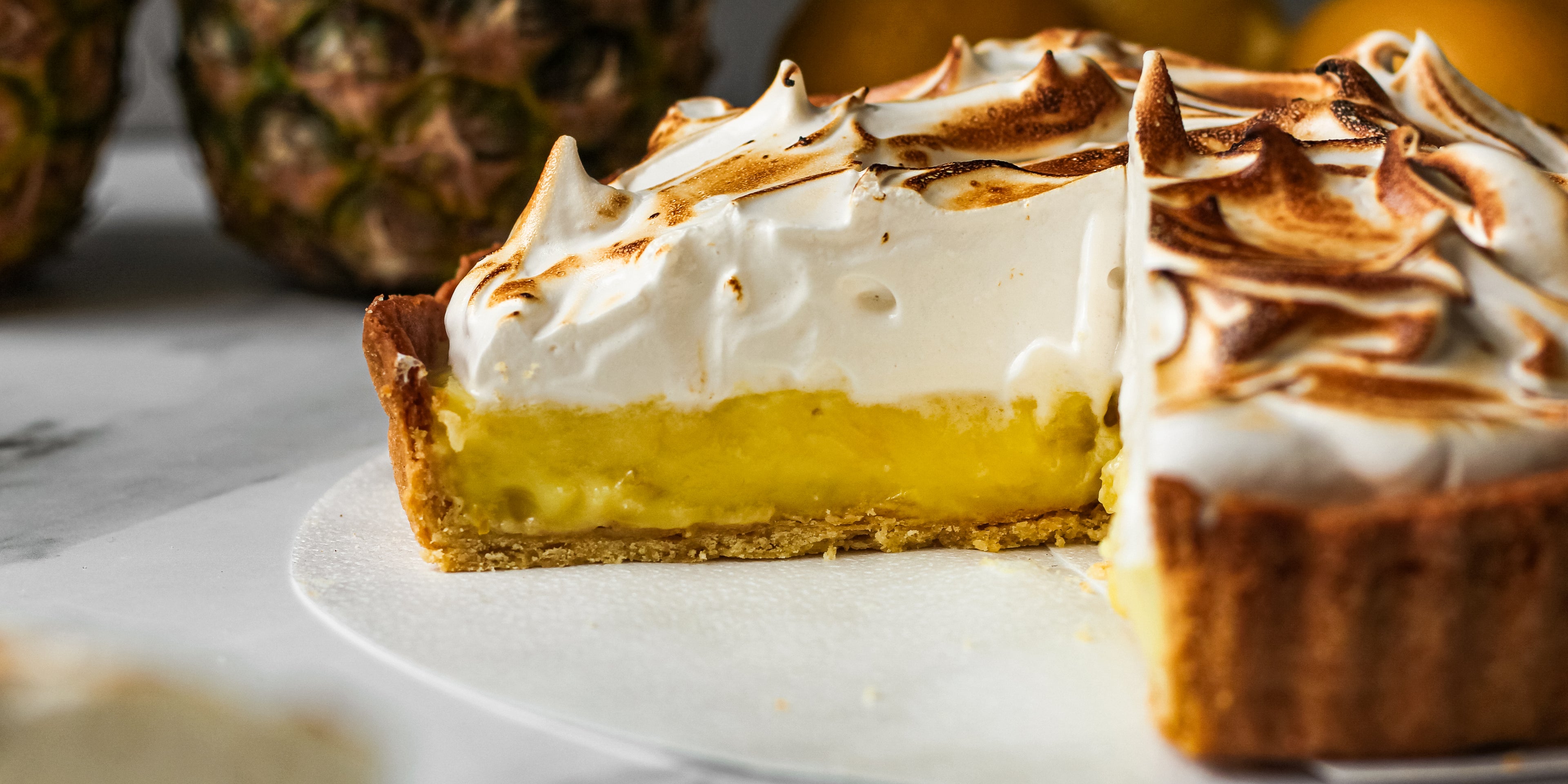Close up of a sliced open Vegan Pineapple Meringue Pie showing the yellow pineapple layer, and thick meringue top