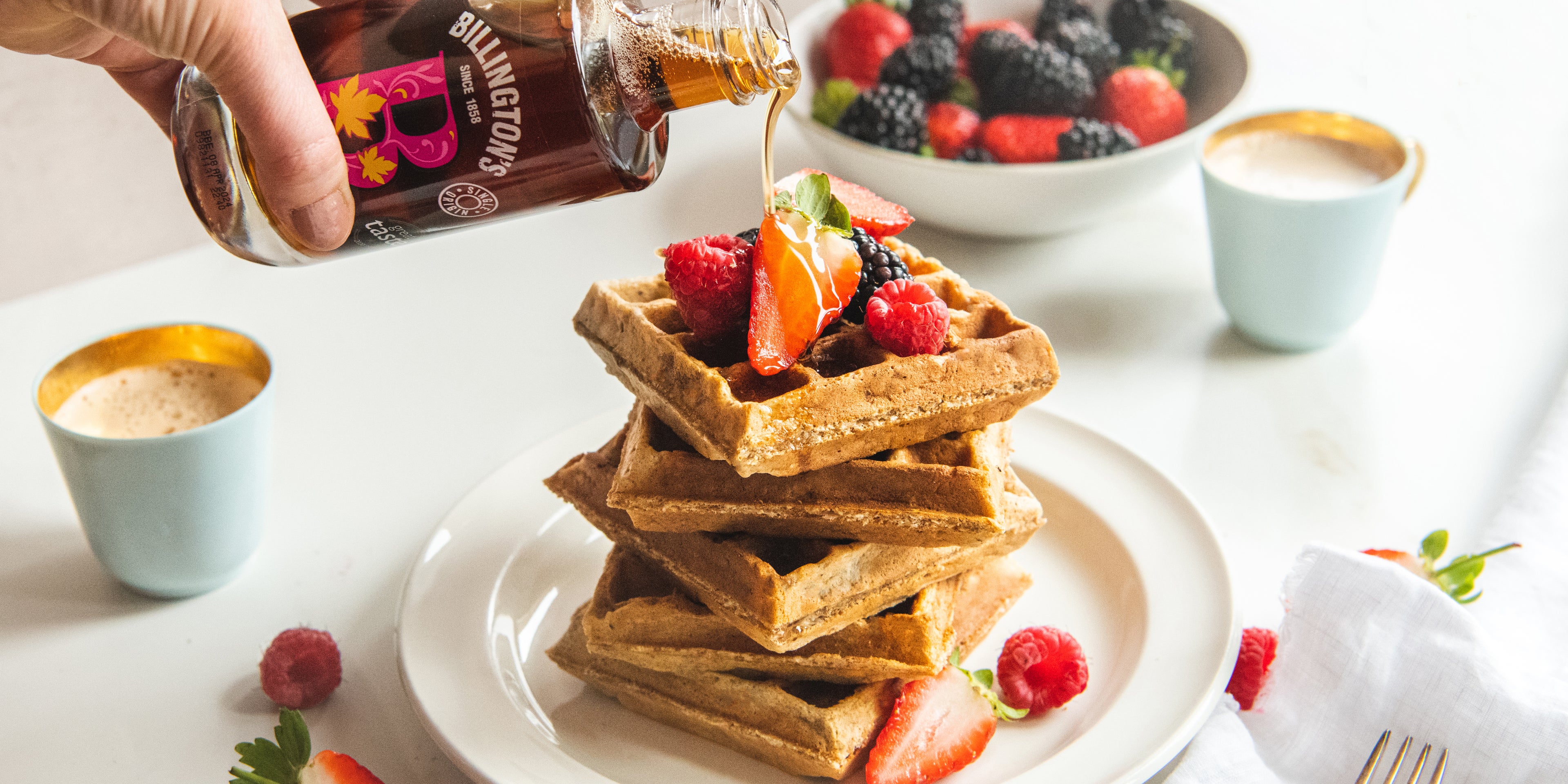 Wholemeal Banana Waffles being drizzled with Billington's maple syrup and topped with berries