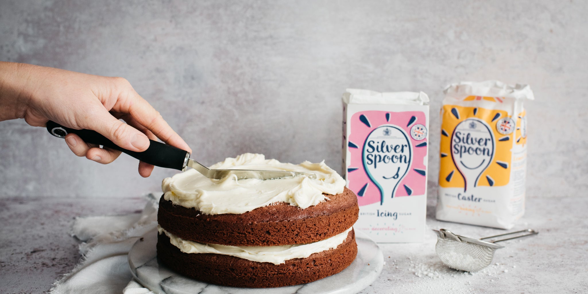 Smoothing vanilla cream cheese frosting over a red velvet cake with a baking spatula 